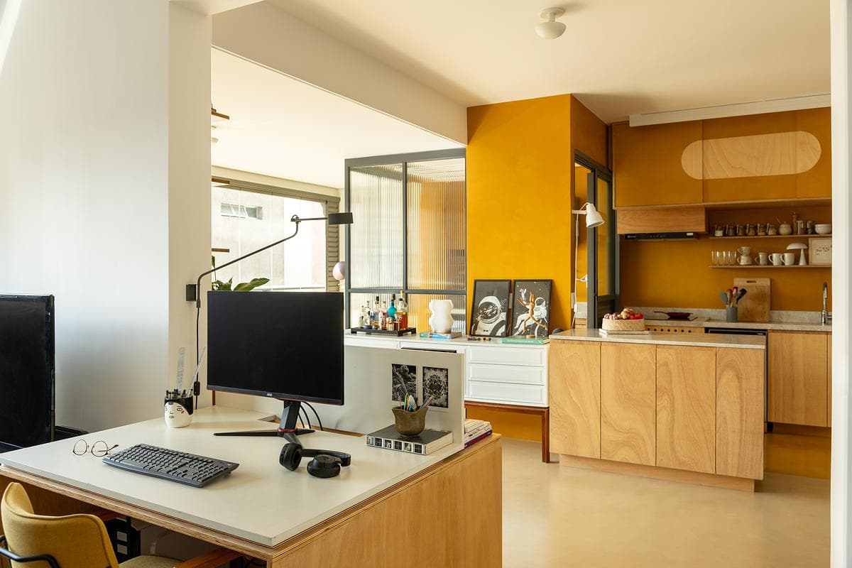A work desk sits alongside the yellow kitchen and its sliding cabinet fronts.