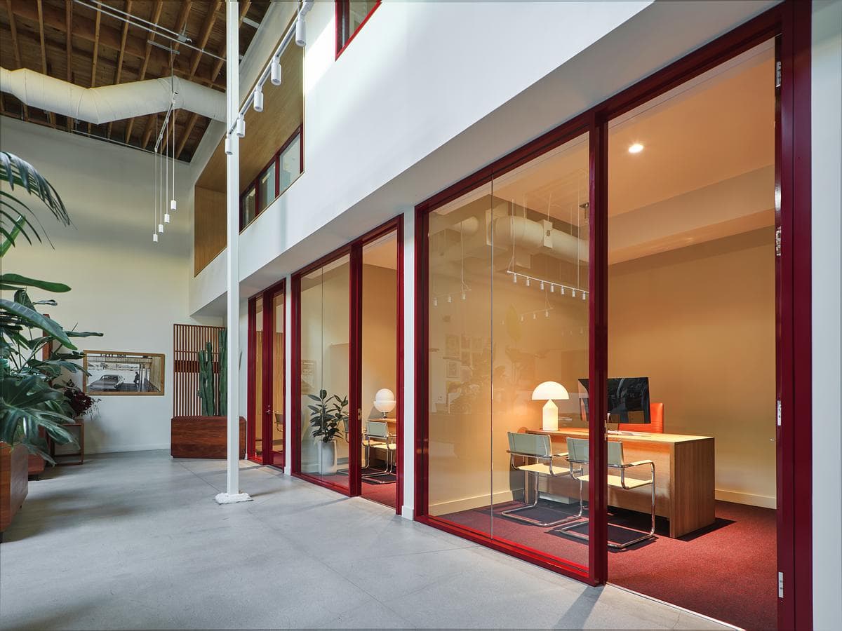 Oxblood-coloured glazing defines a meeting room beside the open office.