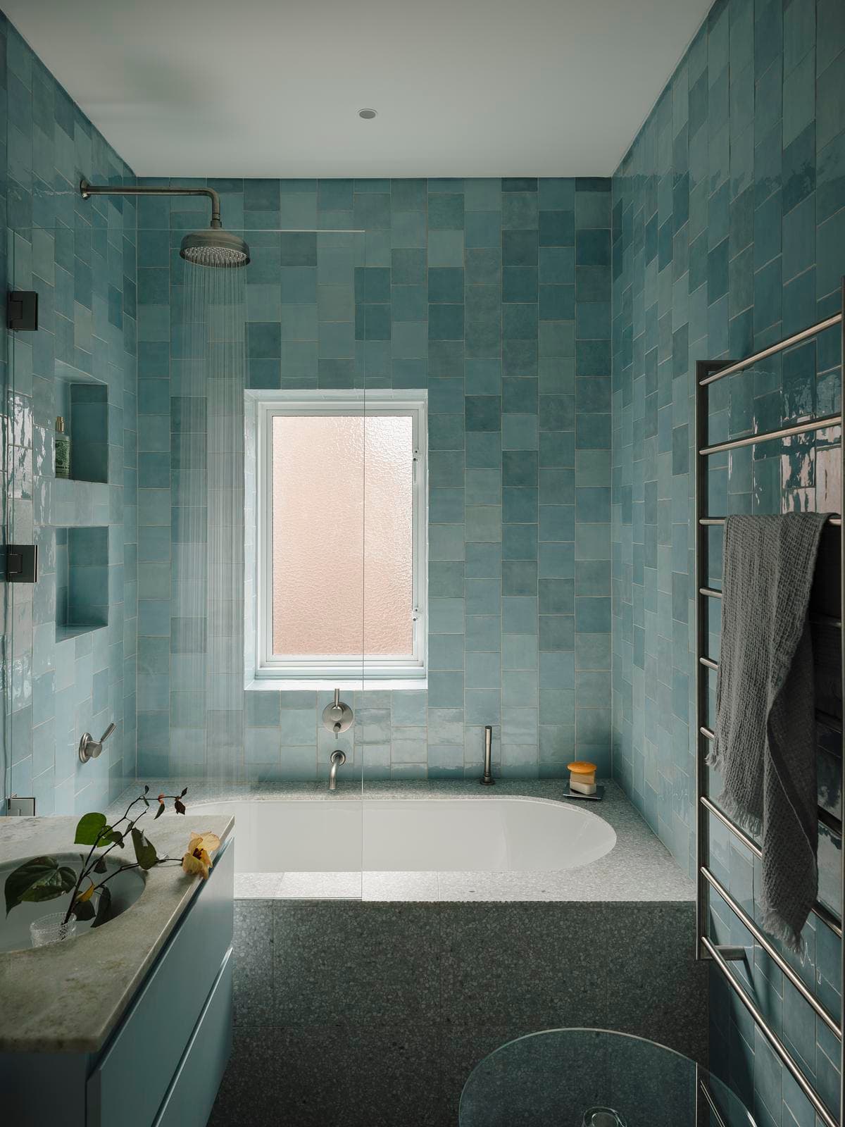 Blue-tiled bathroom with terrazzo and a window above the bath
