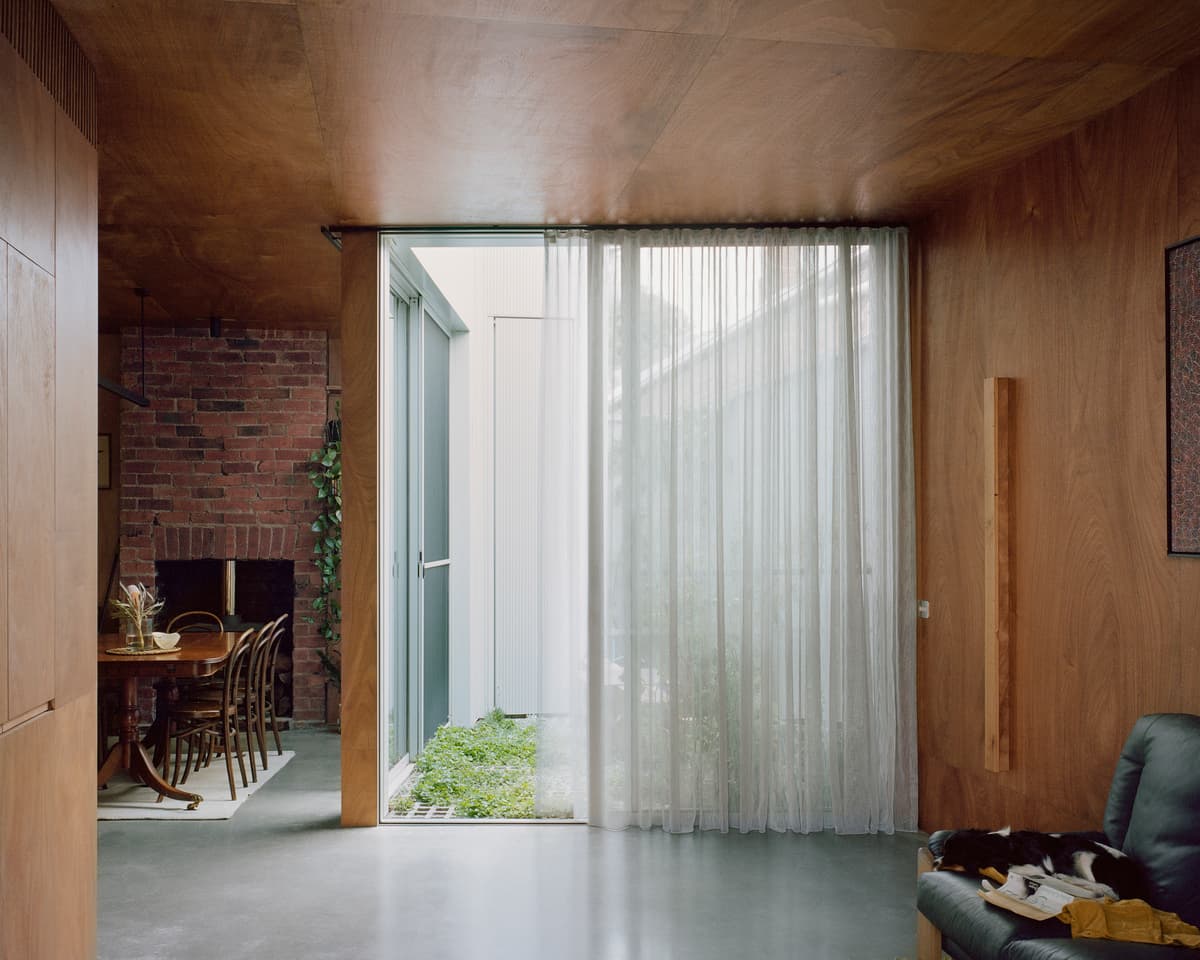 Plywood linings and a glazed courtyard edge bring warmth and daylight to the living room.