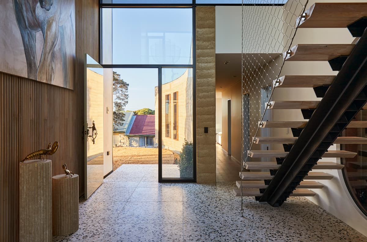 The double-height entrance brings the rammed-earth wall into view from the stair hall.