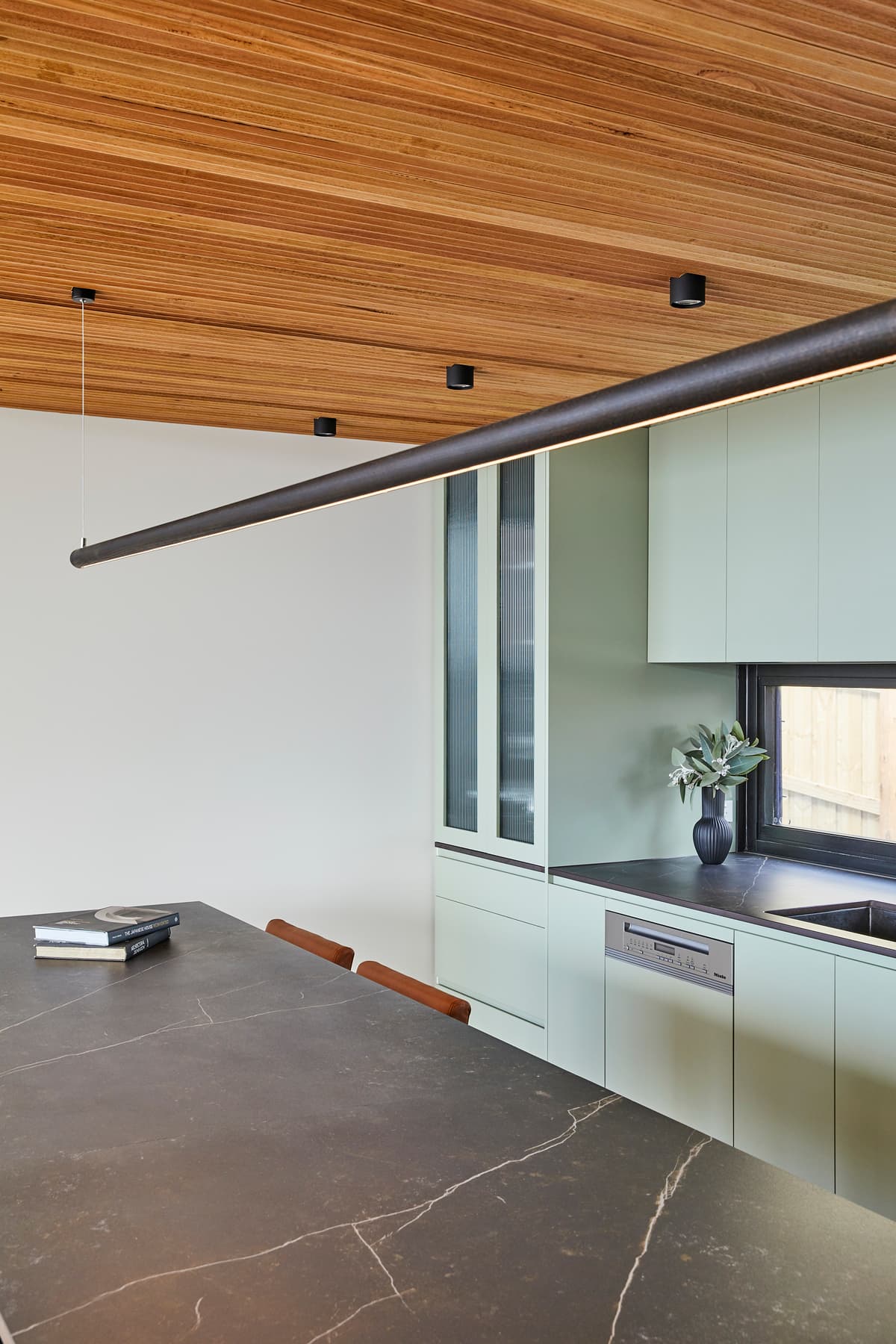 Timber lines the kitchen ceiling above pale cabinetry and a dark worktop.