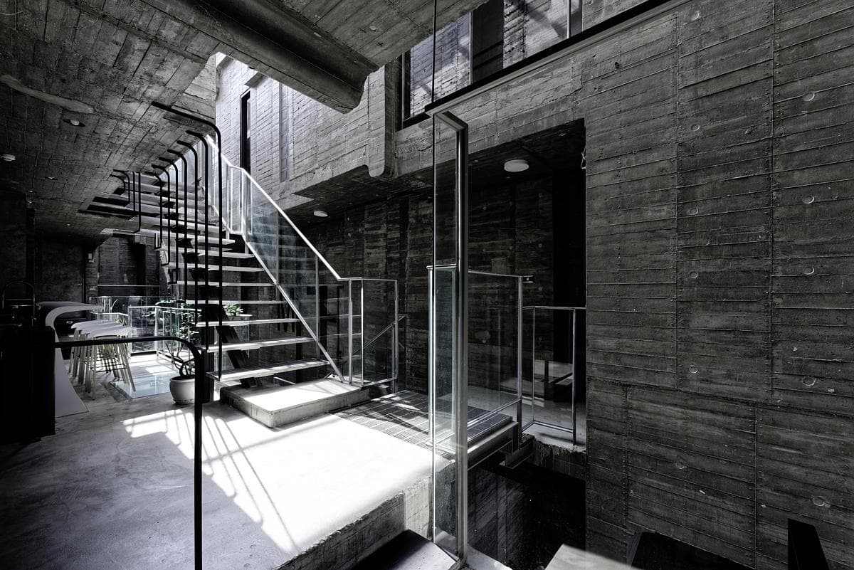 Open steel stair rising through the board-marked concrete courtyard.
