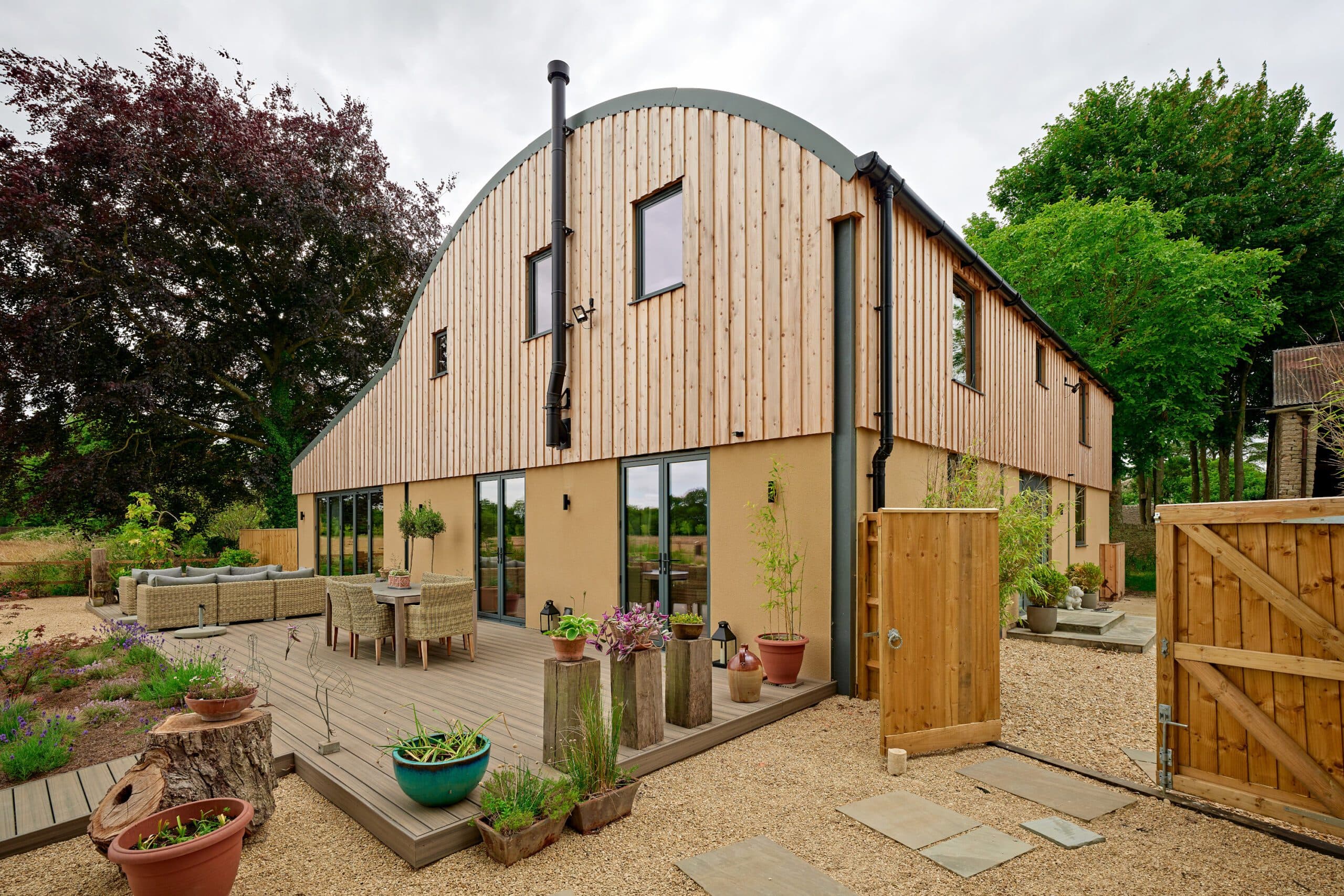 Timber-clad barn conversion with a curved roof, seen from its gravel garden and deck
