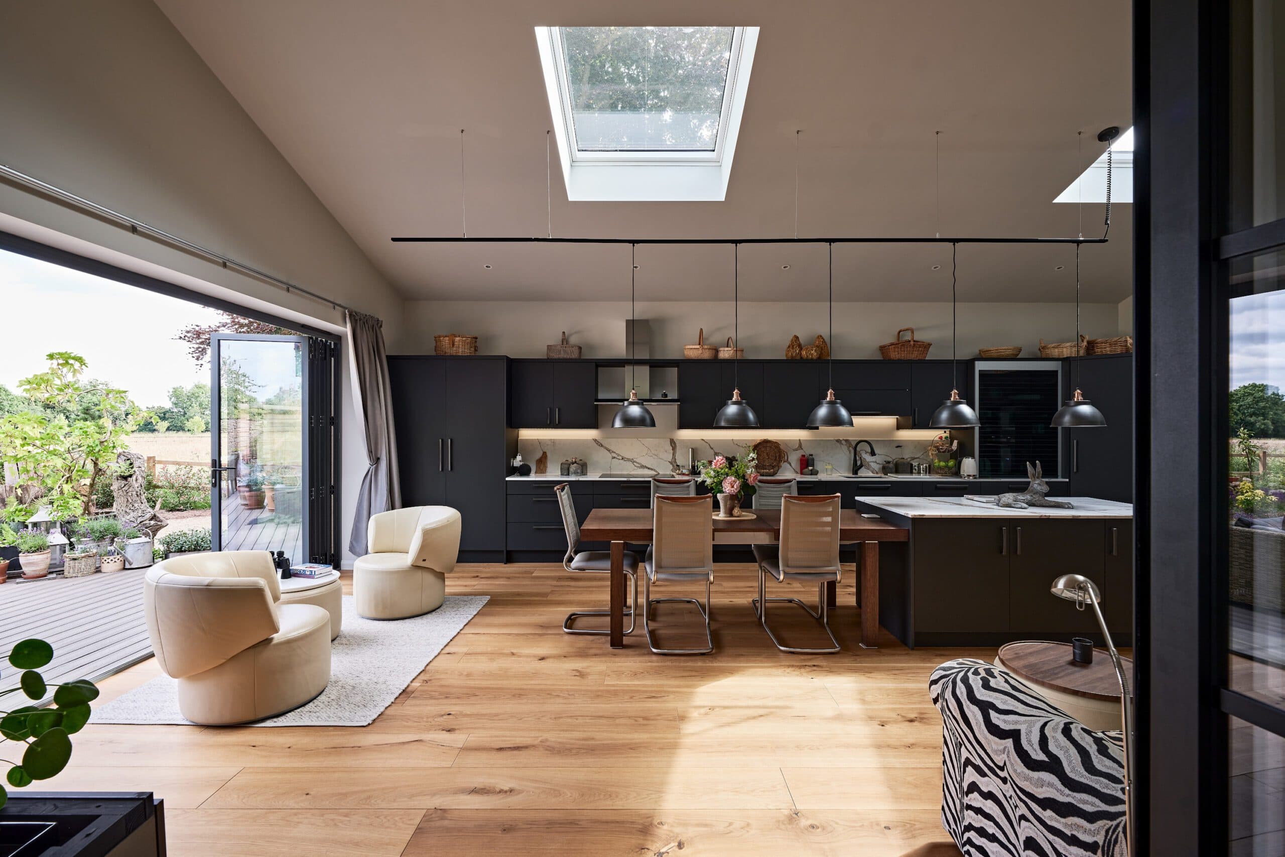 Open-plan kitchen and dining space under a vaulted ceiling with rooflights and folding glass doors