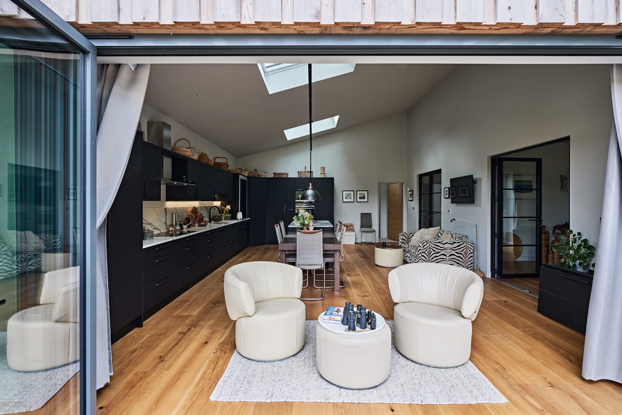 Living area with cream armchairs seen through open sliding doors, with the kitchen beyond