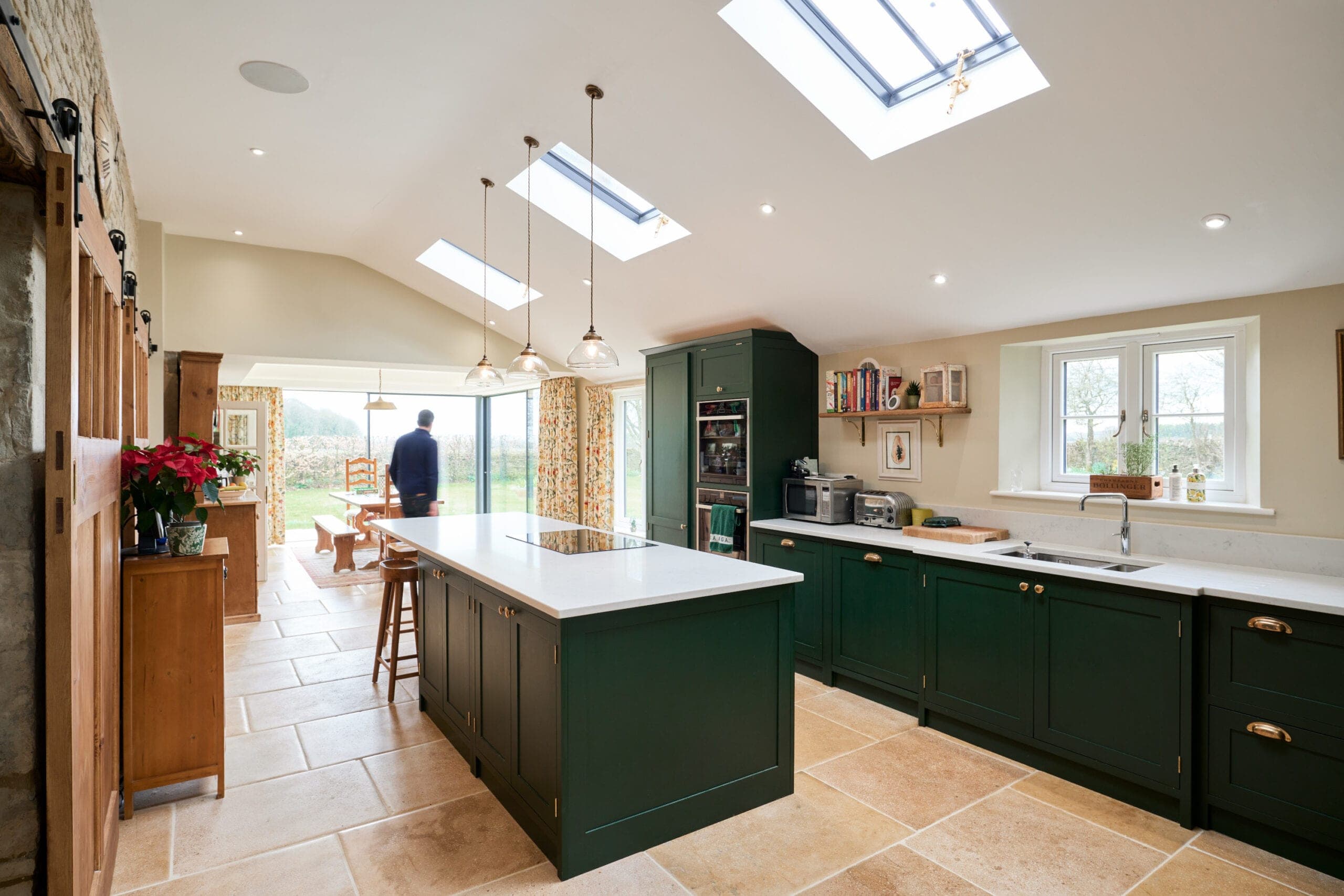 Kitchen with a dark green island and rooflights, with the garden room beyond
