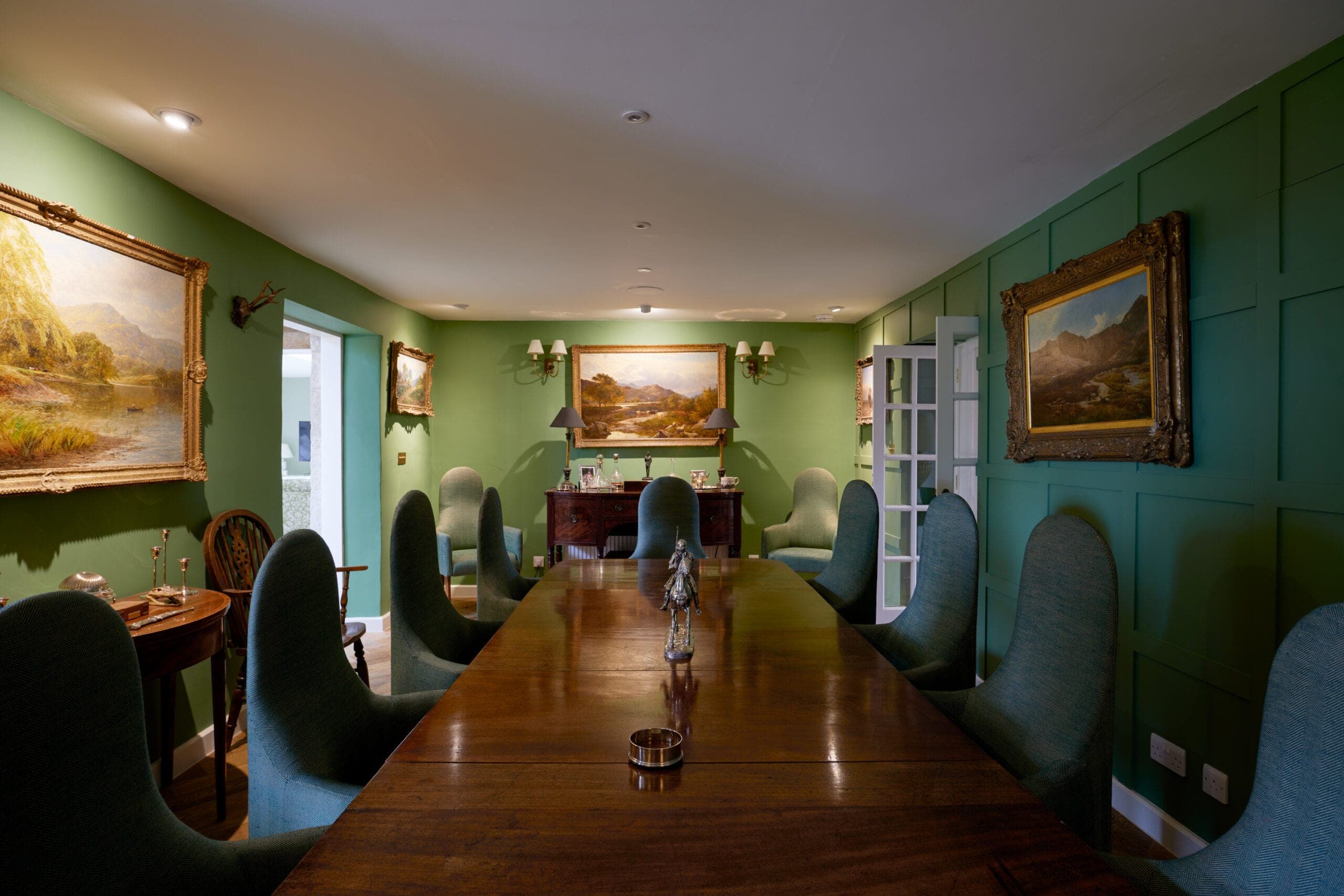 Green-panelled dining room with a long table and landscape paintings