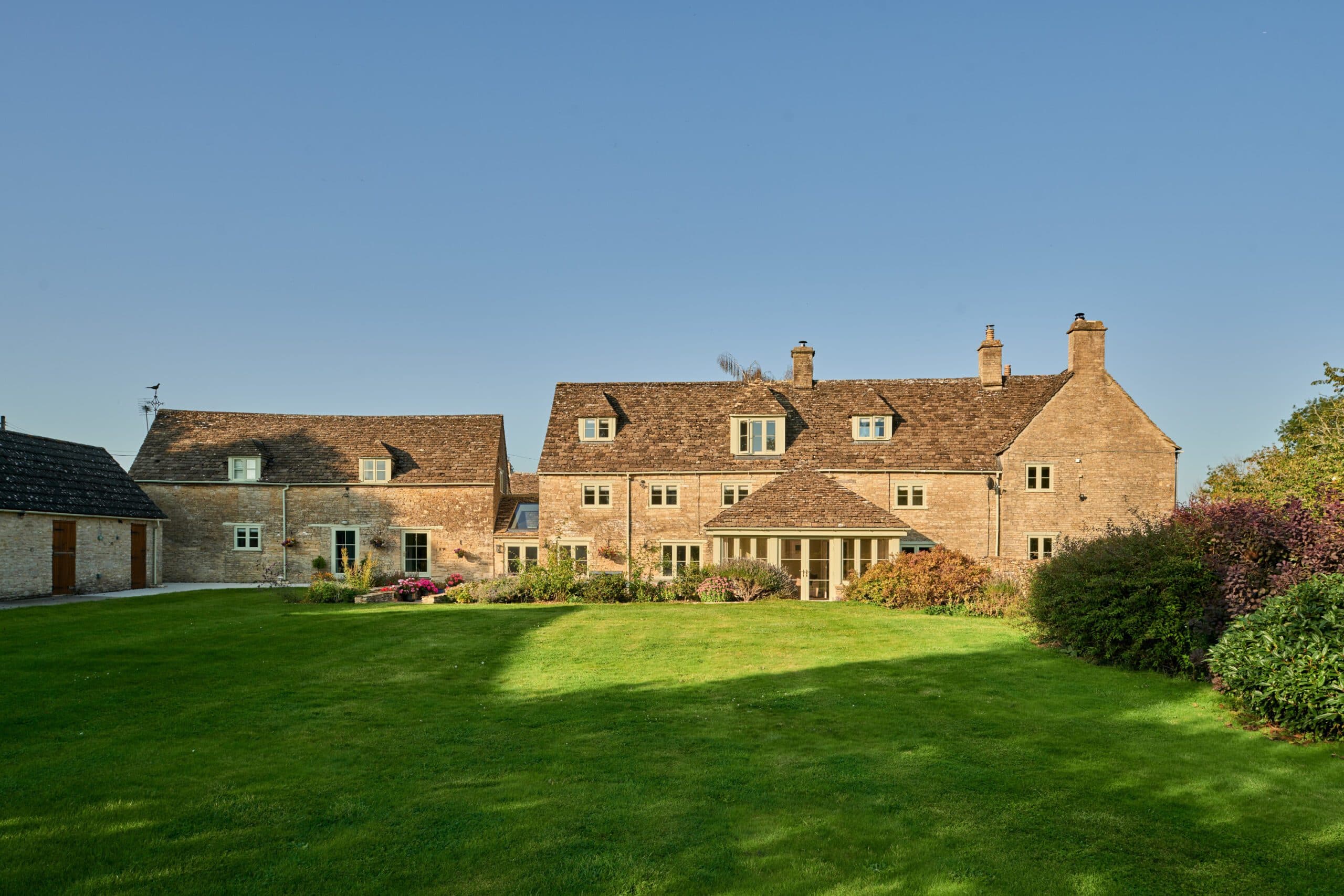 Cotswold stone farmhouse with a garden room, seen across a large lawn