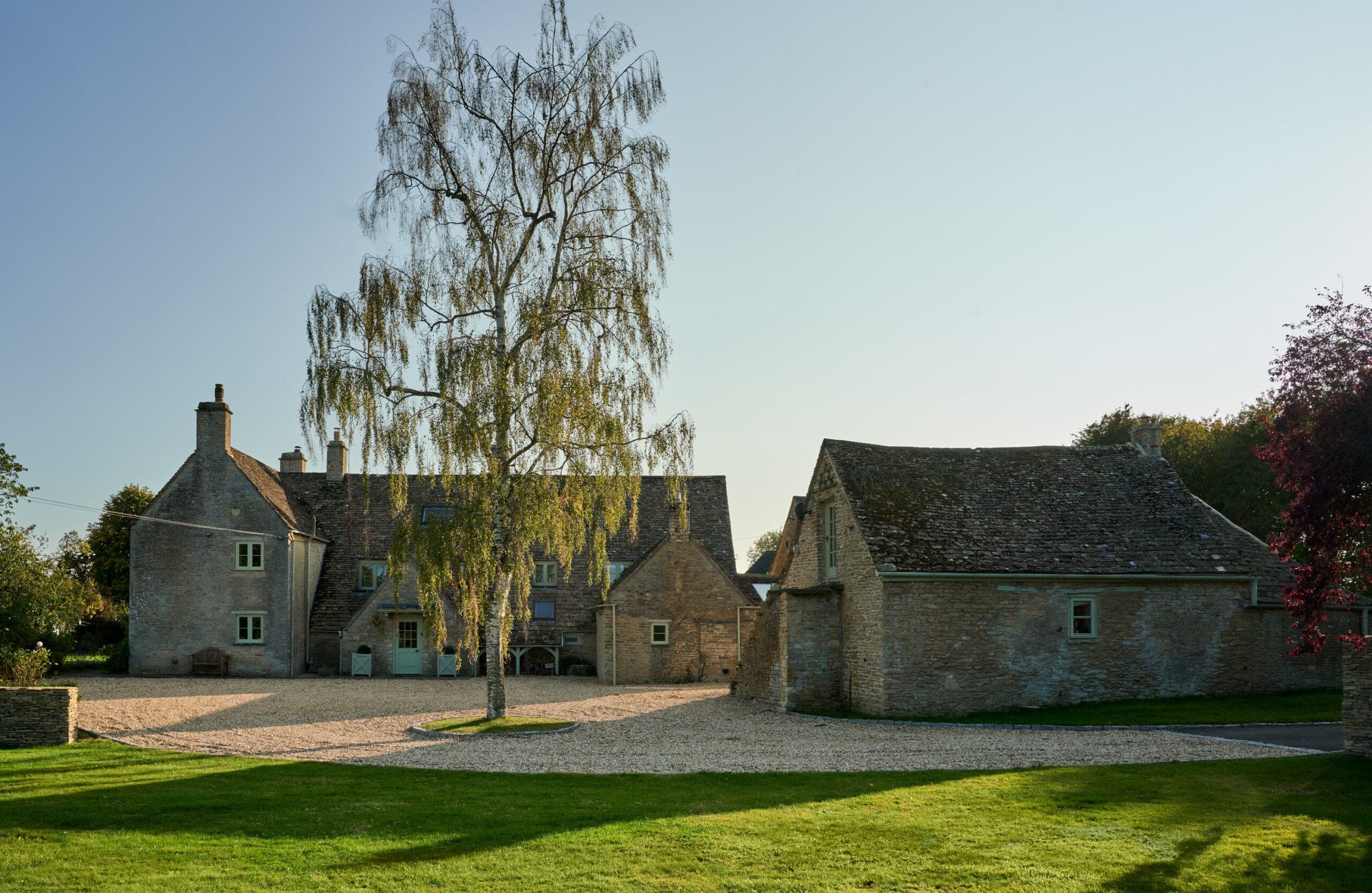Stone farmhouse and outbuilding beside a gravel drive with a silver birch