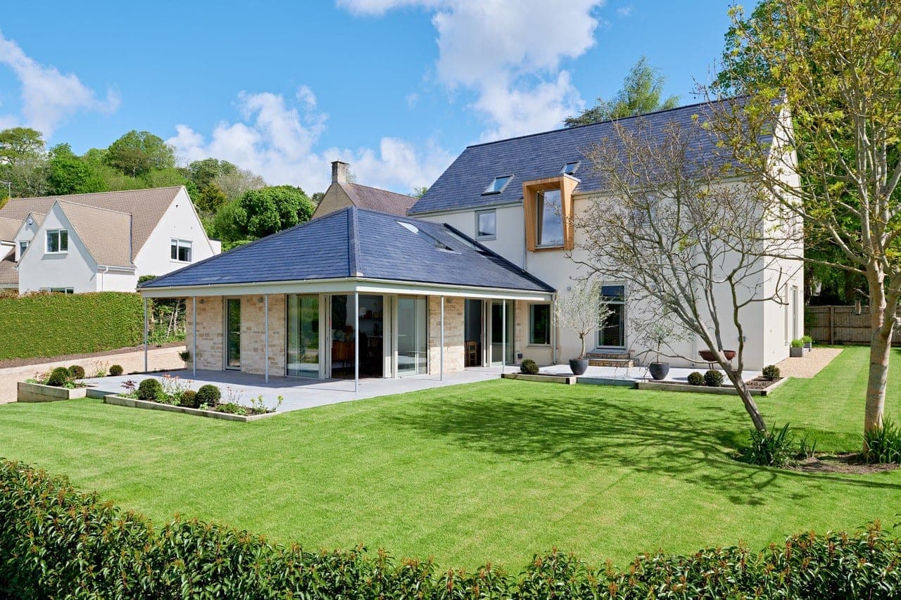 White rendered house with a slate-roofed single-storey wing and a timber-framed window, seen across a lawn