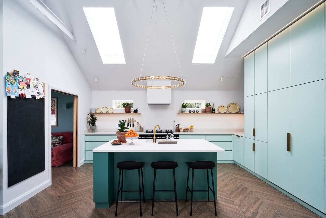 Kitchen with a green island, pale blue tall units and rooflights in a vaulted ceiling