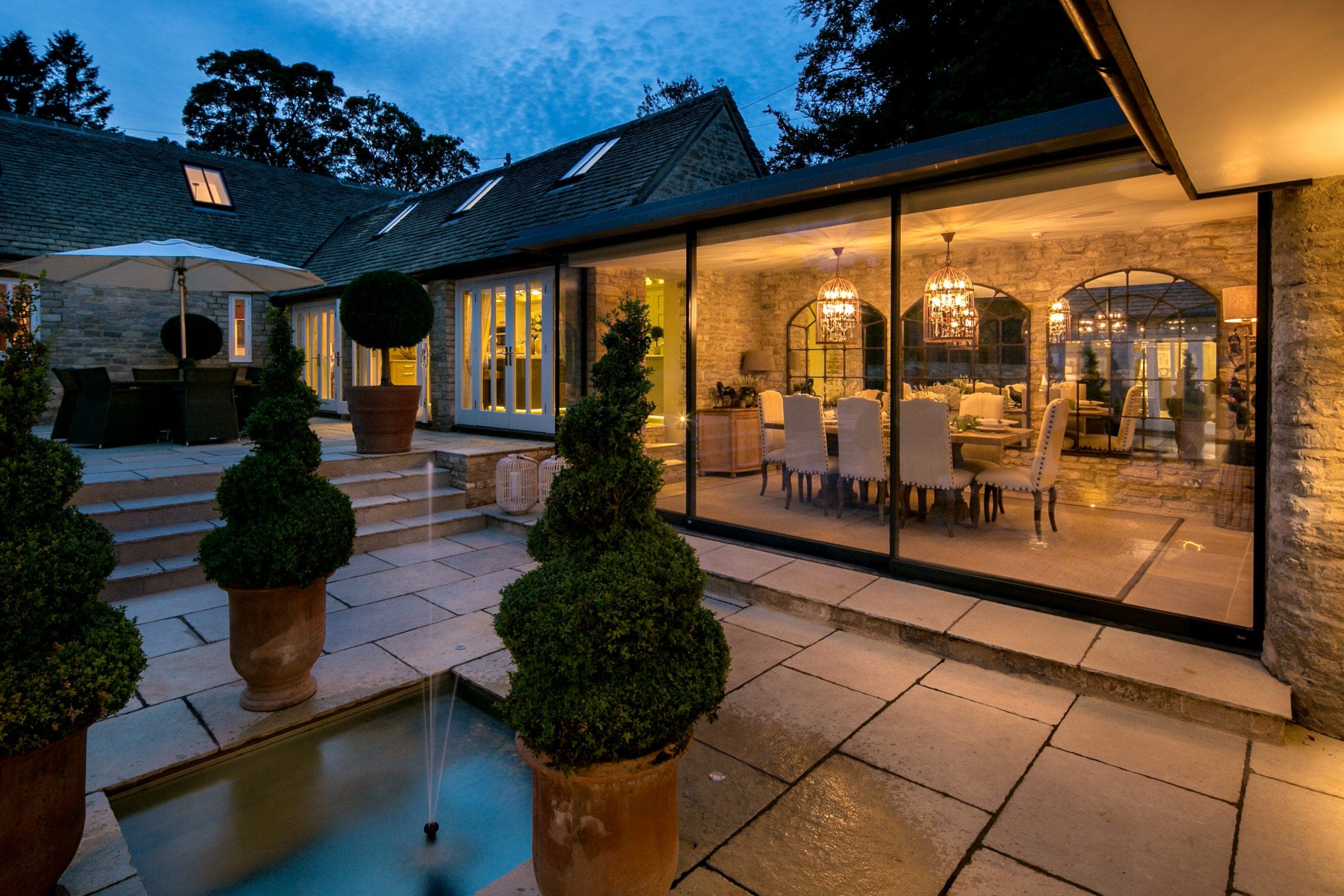 Courtyard at dusk with a lit dining room behind a wall of sliding glass