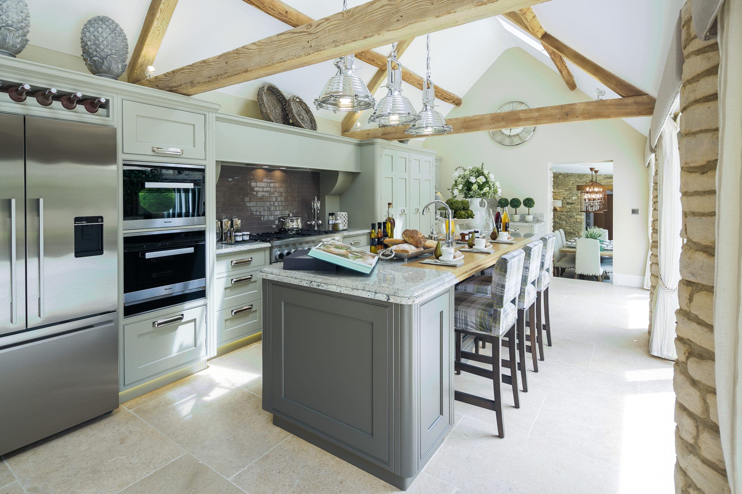 Kitchen with sage-green units, a stone-topped island and exposed roof timbers