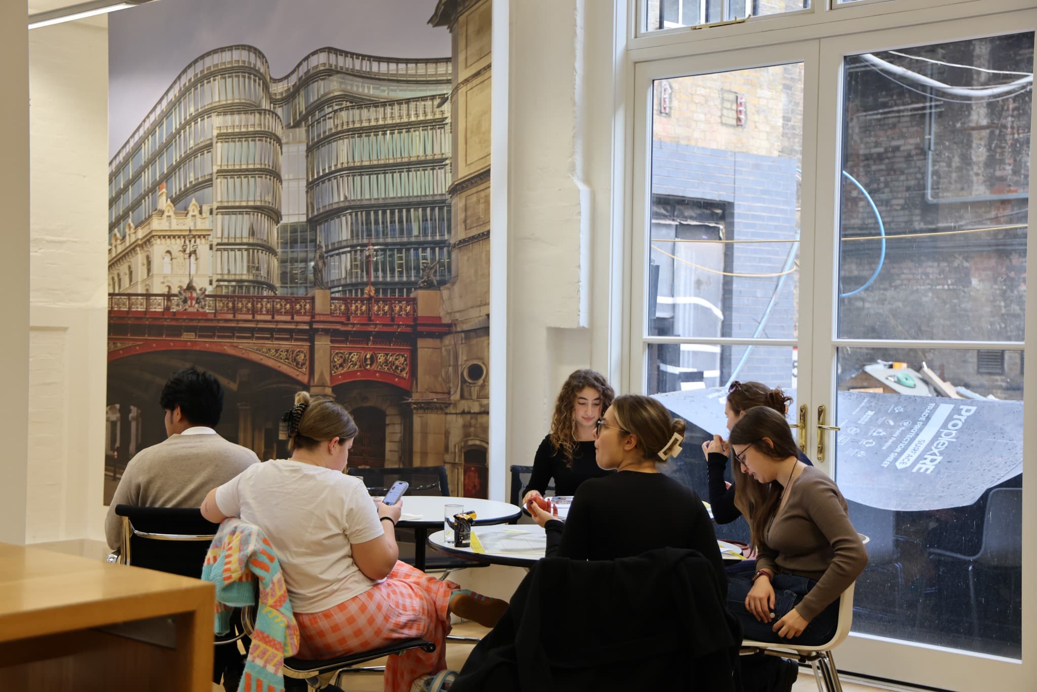 A group discussing design work beside a large architectural mural.