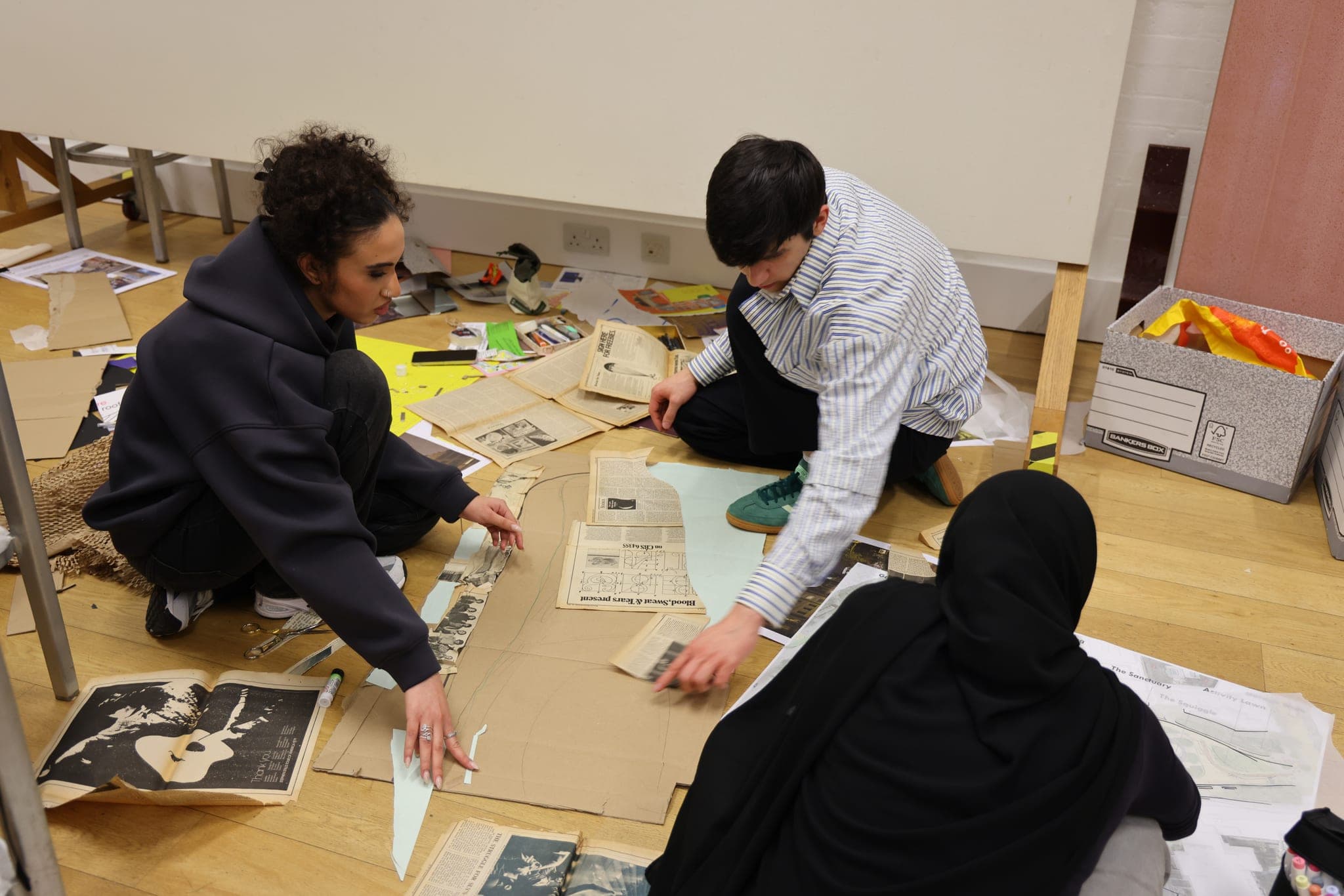 Three participants assembling a design with paper and card on the floor.