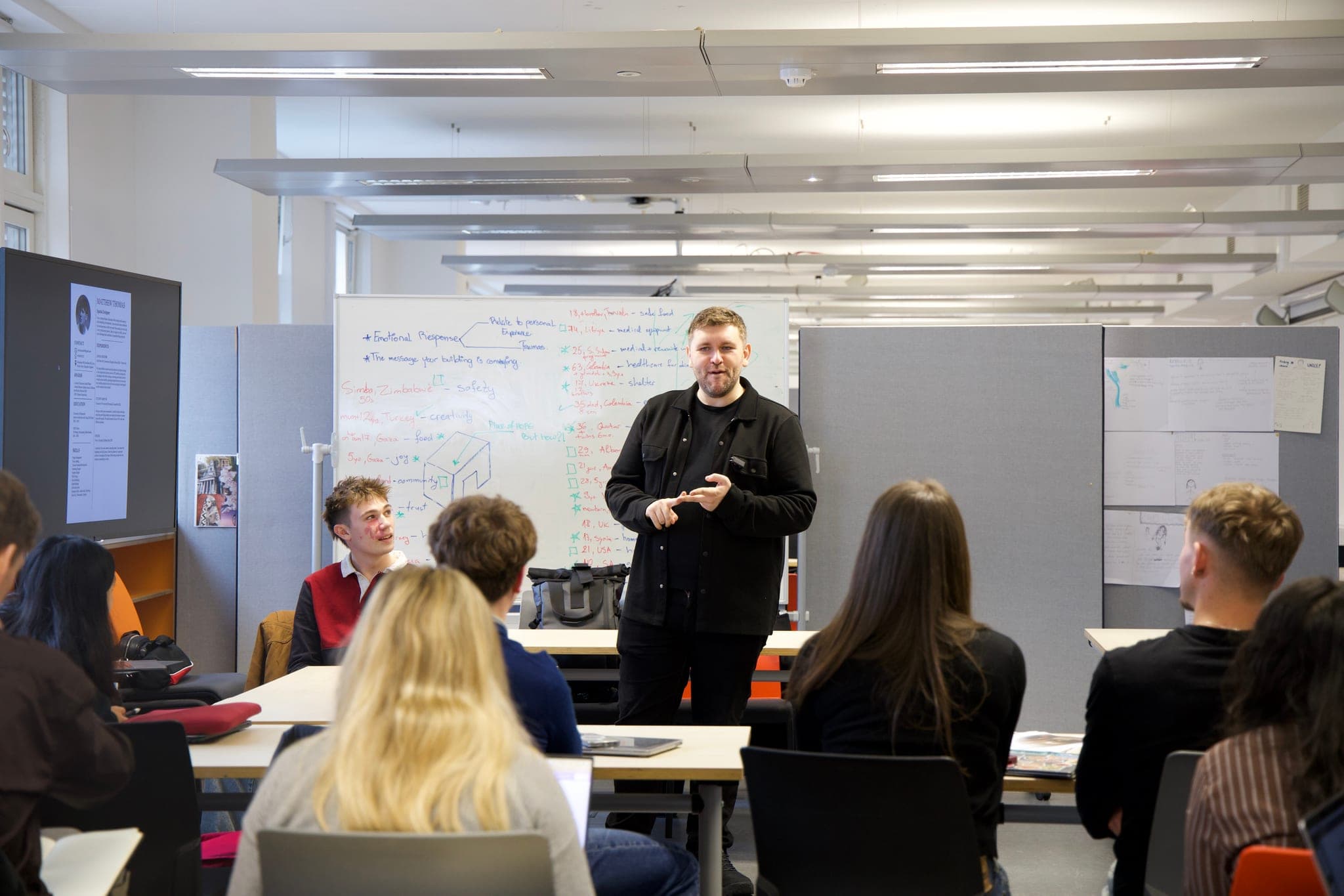 A speaker addressing seated workshop participants beside a whiteboard.