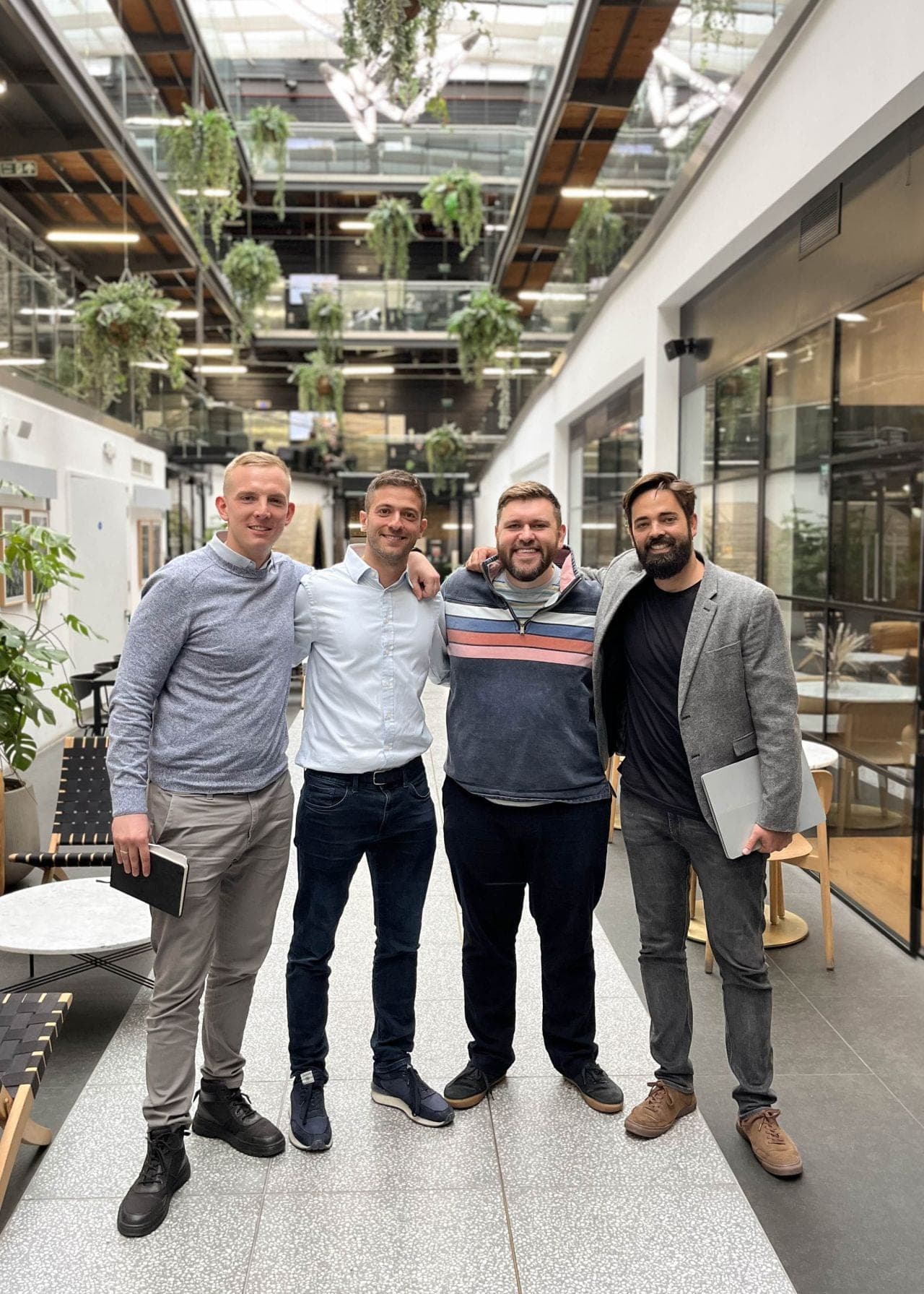 Four people standing together in a bright atrium with planted balconies.