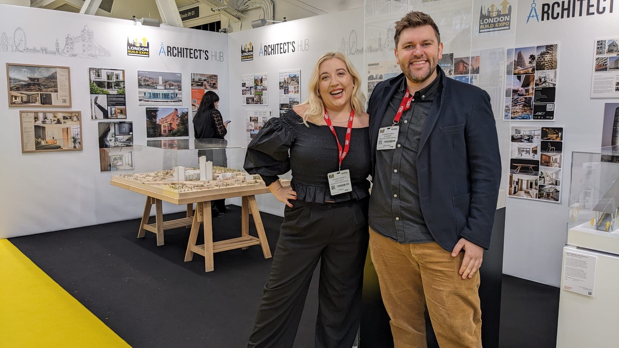 Two people beside architectural models and project displays at an exhibition.