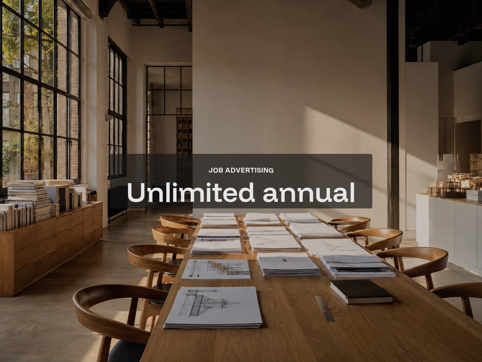 Unlimited annual job advertising cover: a long oak meeting table of drawings in late-day studio light.