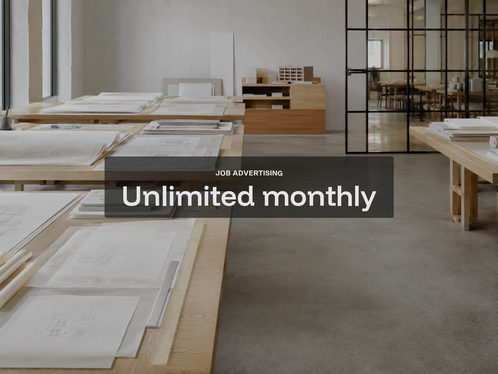 Unlimited monthly job advertising cover: rows of oak desks with stacked drawings in a quiet studio.