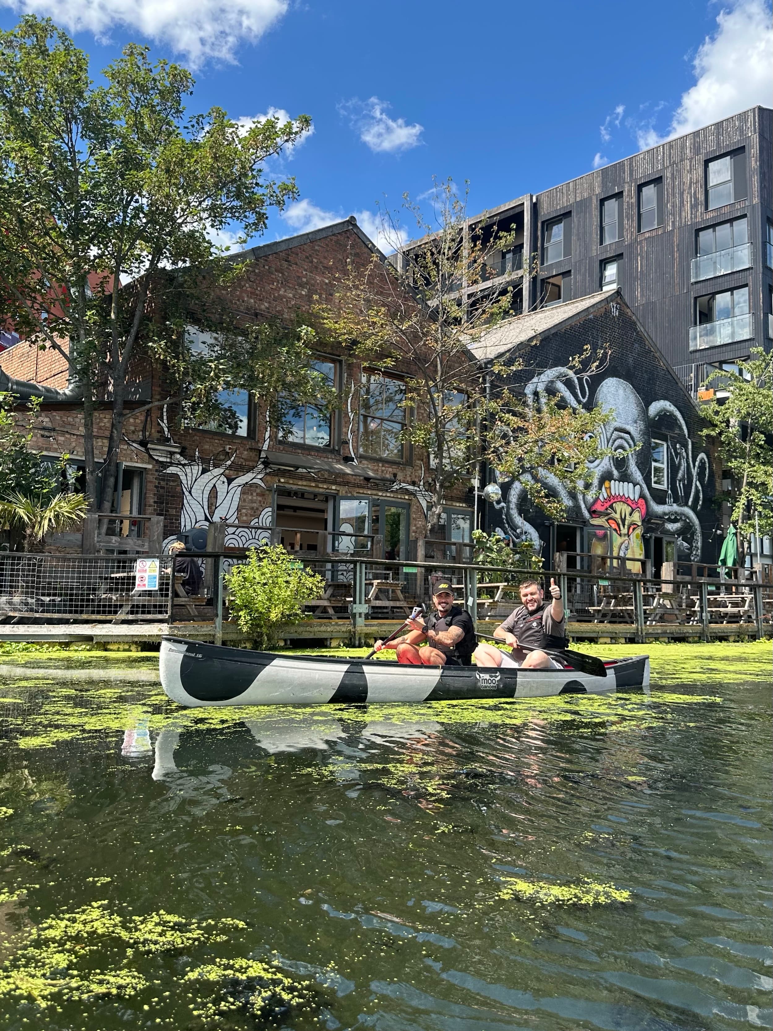 Colleagues smiling and giving a thumbs up together in a canoe