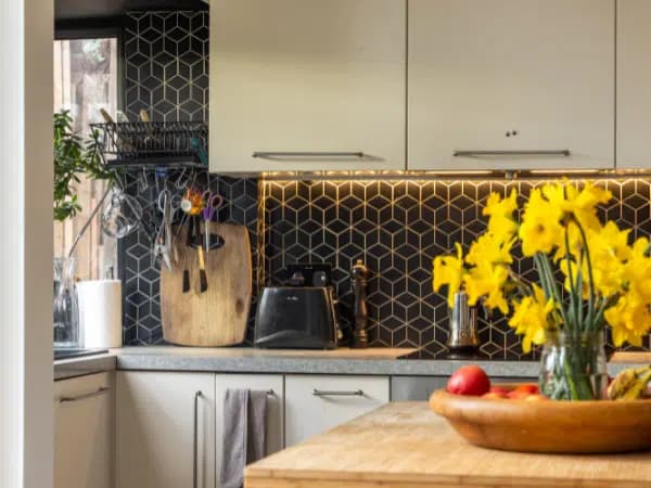 Kitchen at Magda’s Stretford home, with green cabinets and a black tiled splashback