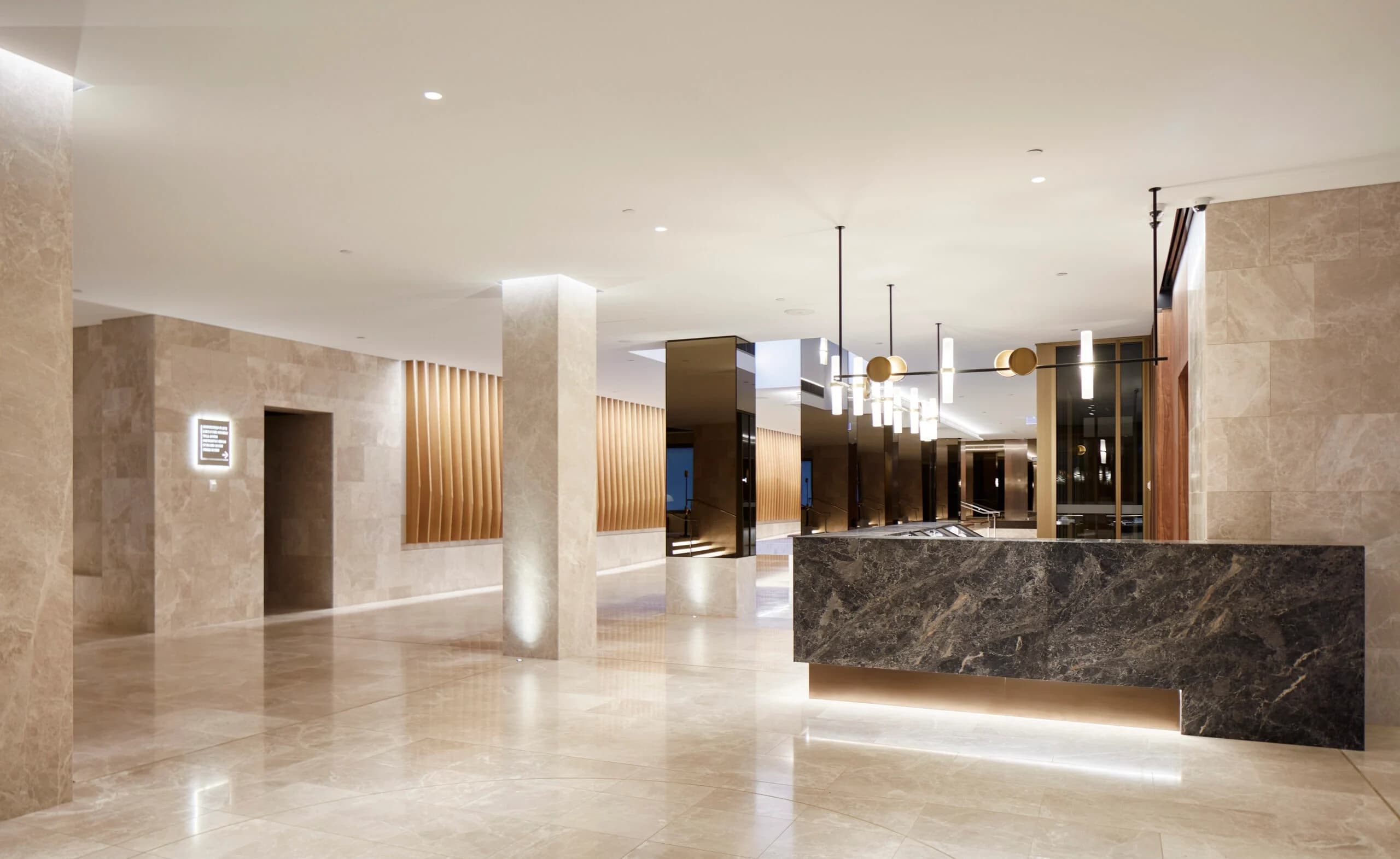 Stone reception desk and pale tiled lobby with columns, timber panels and pendant lights.