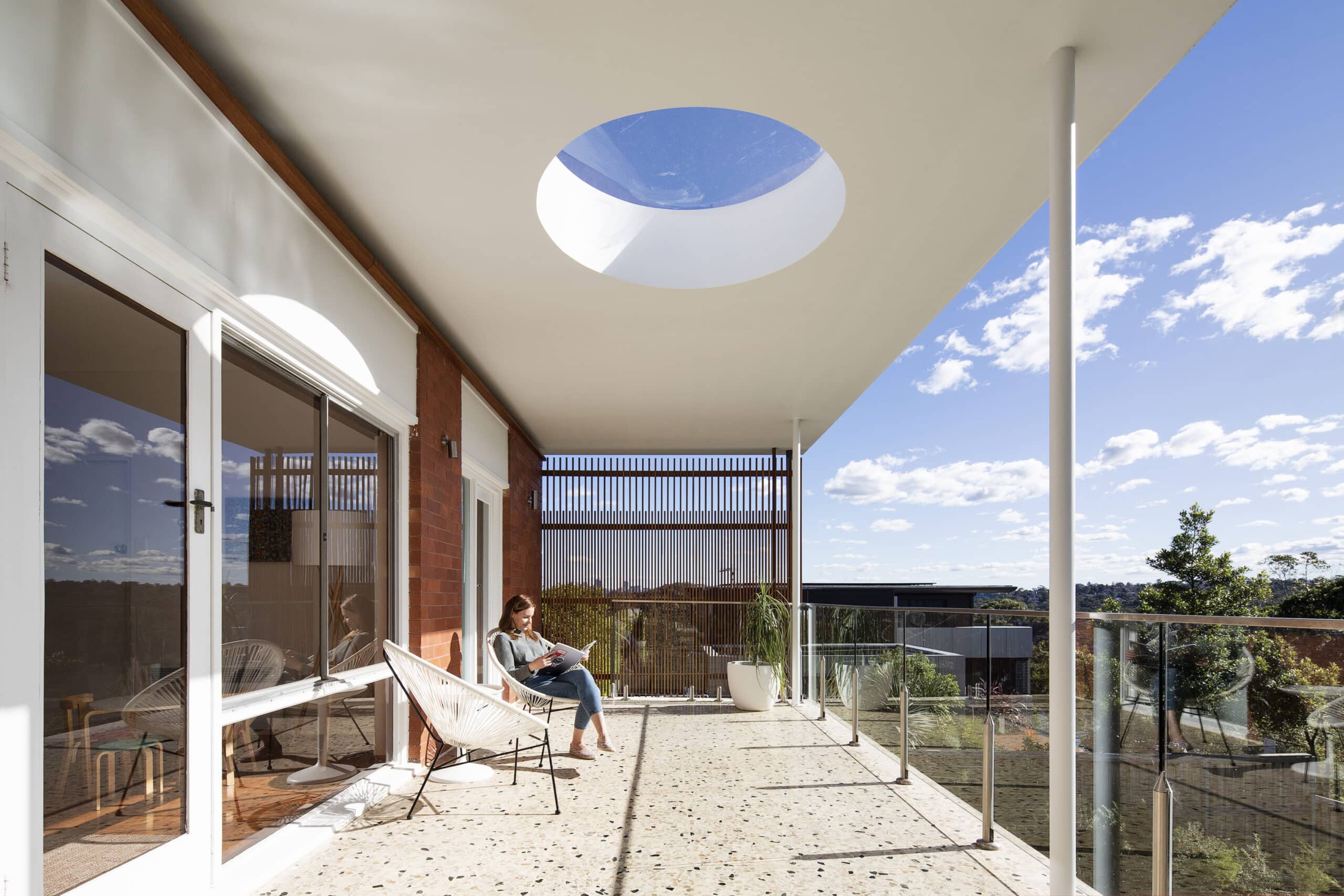 Covered terrace with a circular roof opening, slender columns and a glass balustrade.