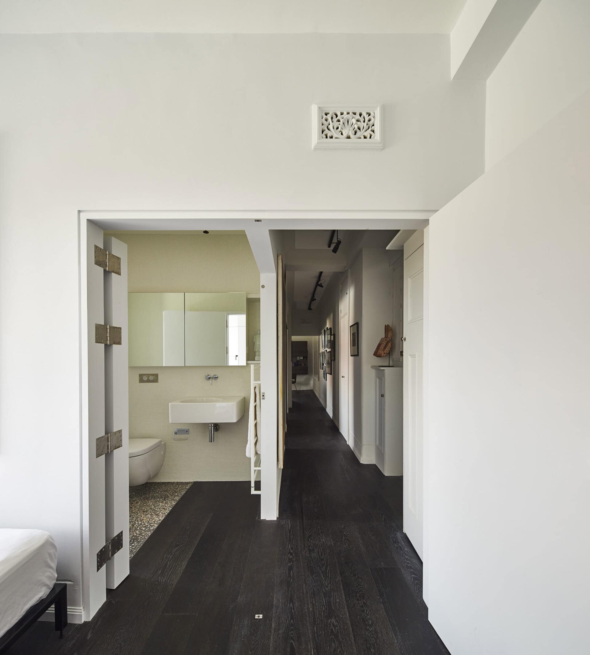 White-painted apartment interior with dark timber flooring and glazed doors opening onto a corridor and bathroom.