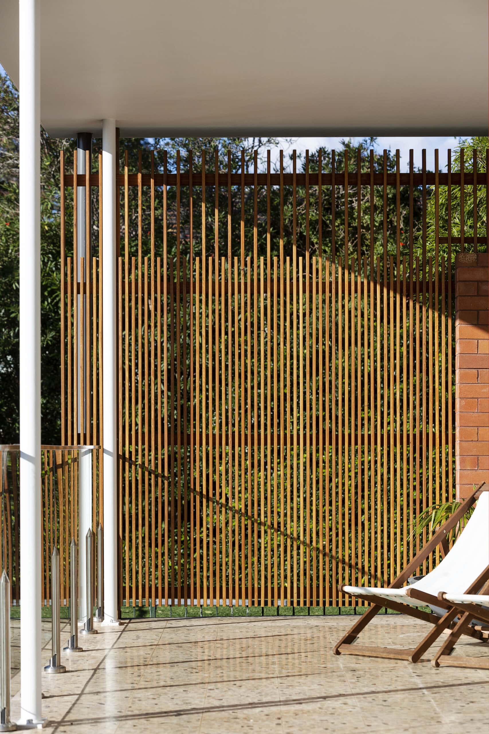 Vertical timber screening at the end of a terrace beside brickwork and a deck chair.