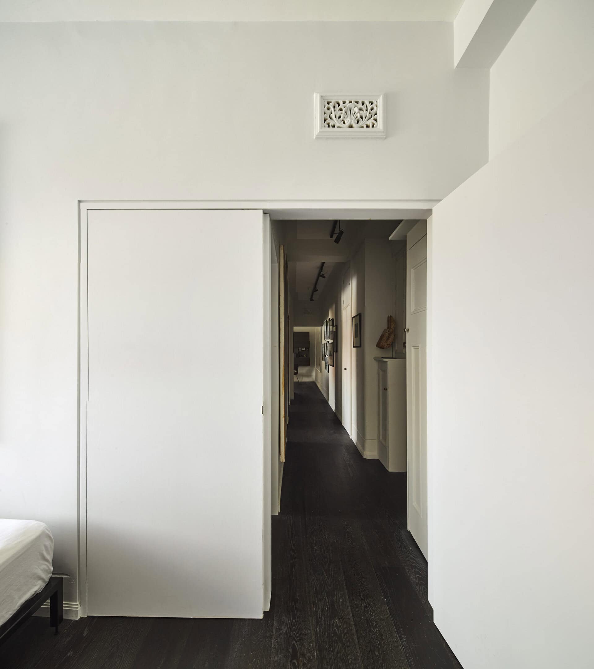 White bedroom wall and sliding doorway opening onto the apartment's dark-floored corridor.