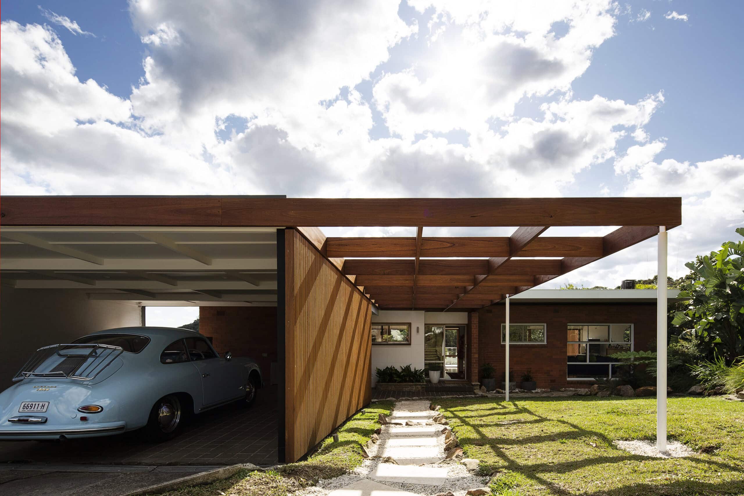 Timber entrance canopy beside a covered carport, stone path and front lawn.