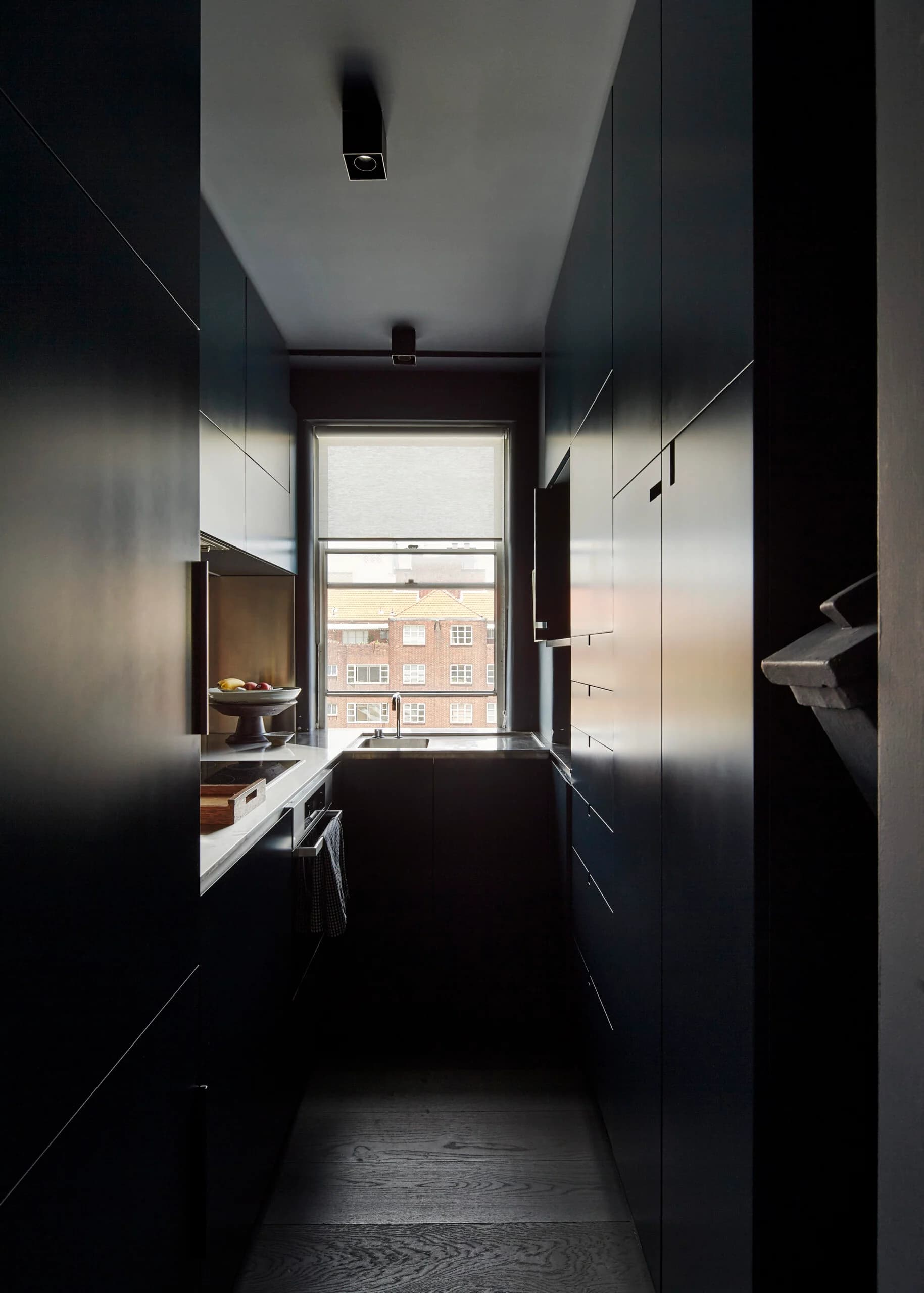 Narrow dark galley kitchen with a window looking towards a neighbouring brick building.