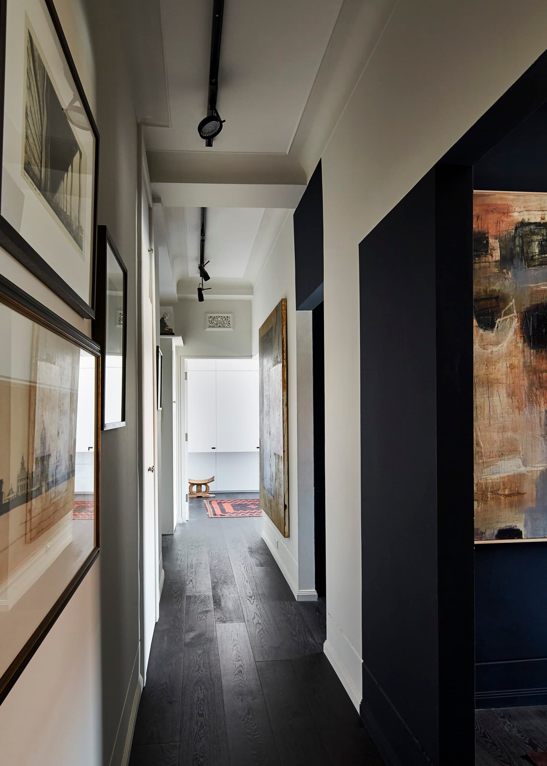 Long white corridor with dark timber flooring, framed artworks and black door recesses.