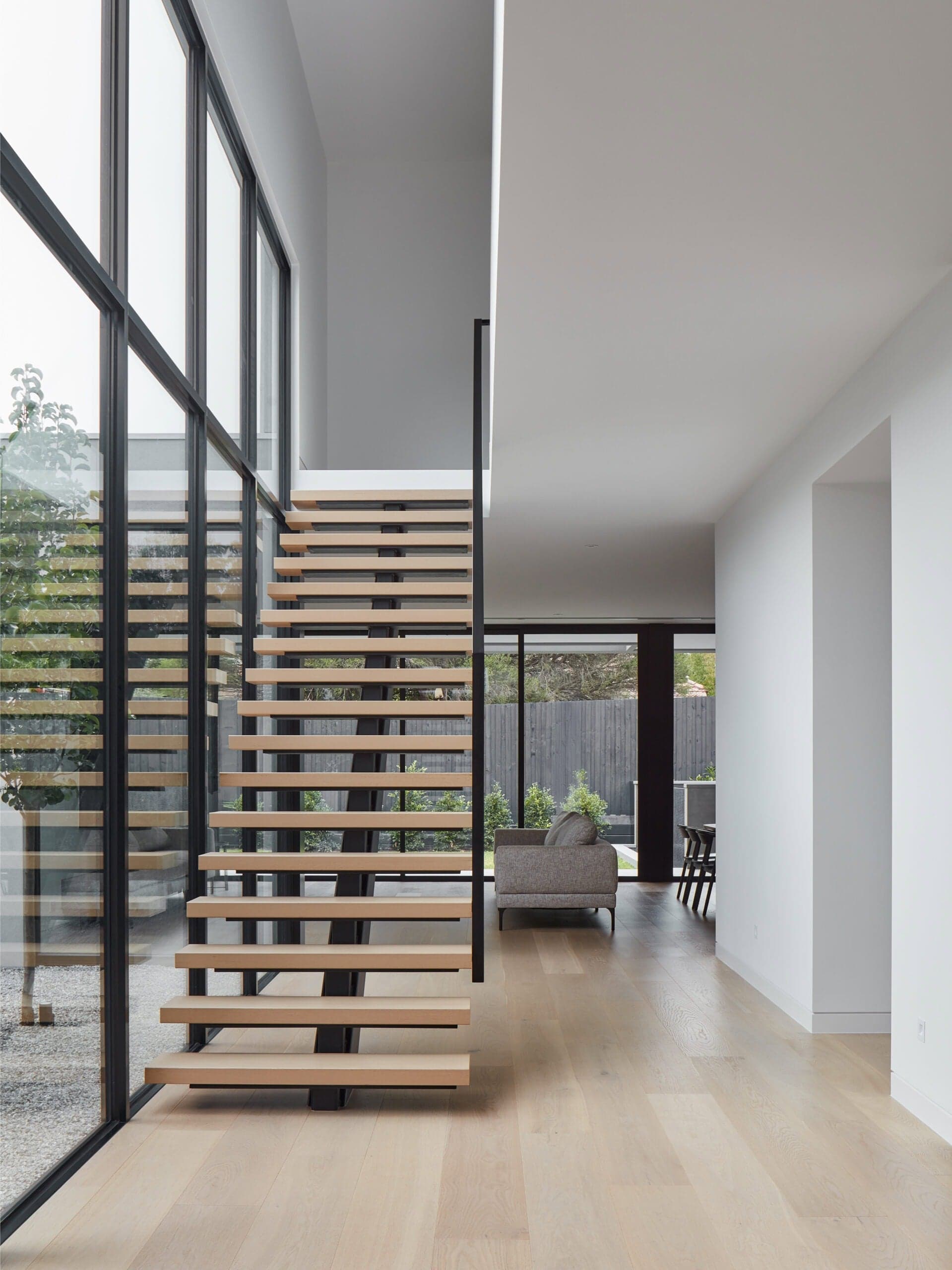 Open-tread timber staircase beside full-height glazing, overlooking the living space at Vincent House.