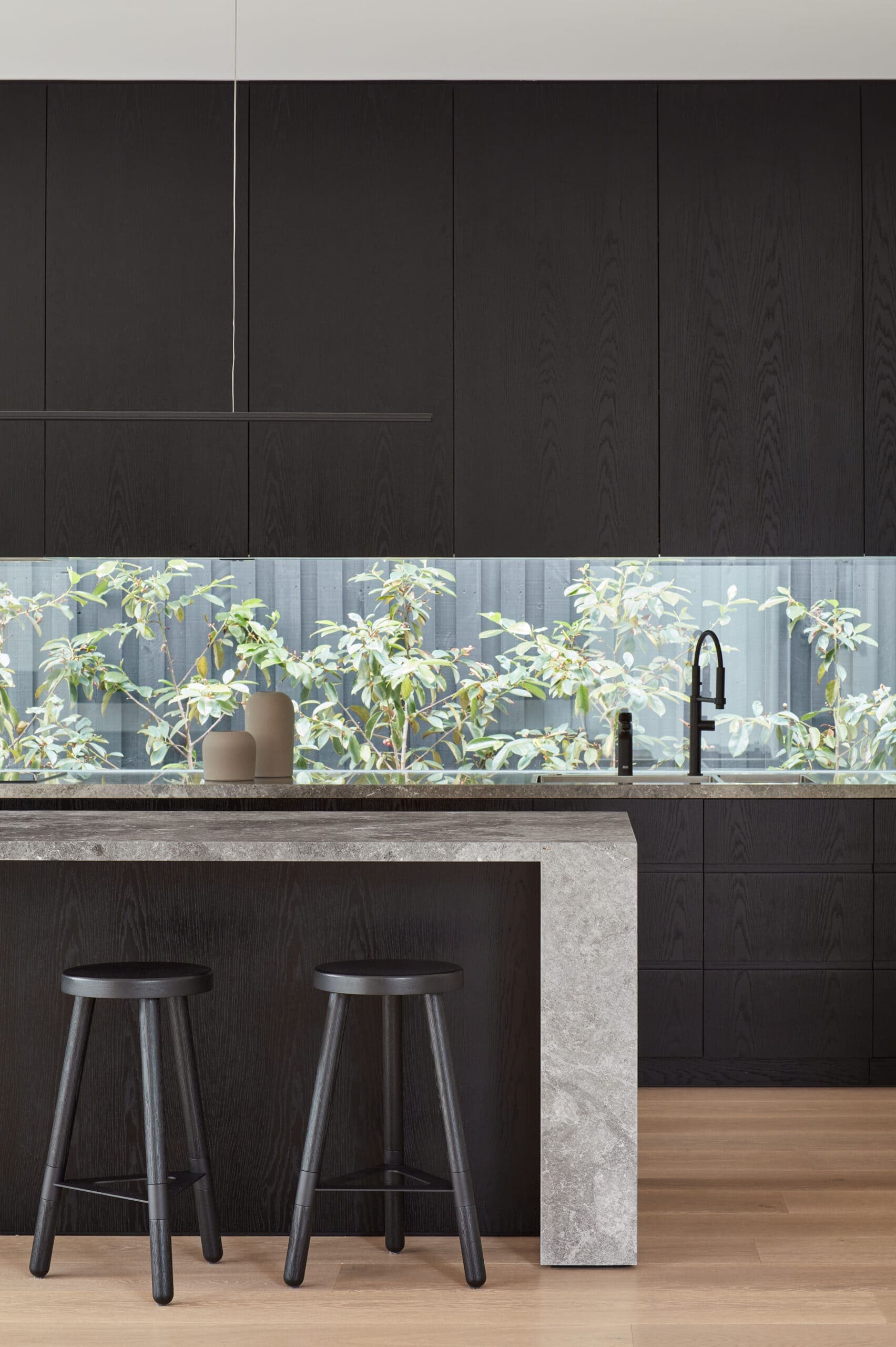 Dark timber kitchen cabinetry above a narrow glazed splashback overlooking planting.