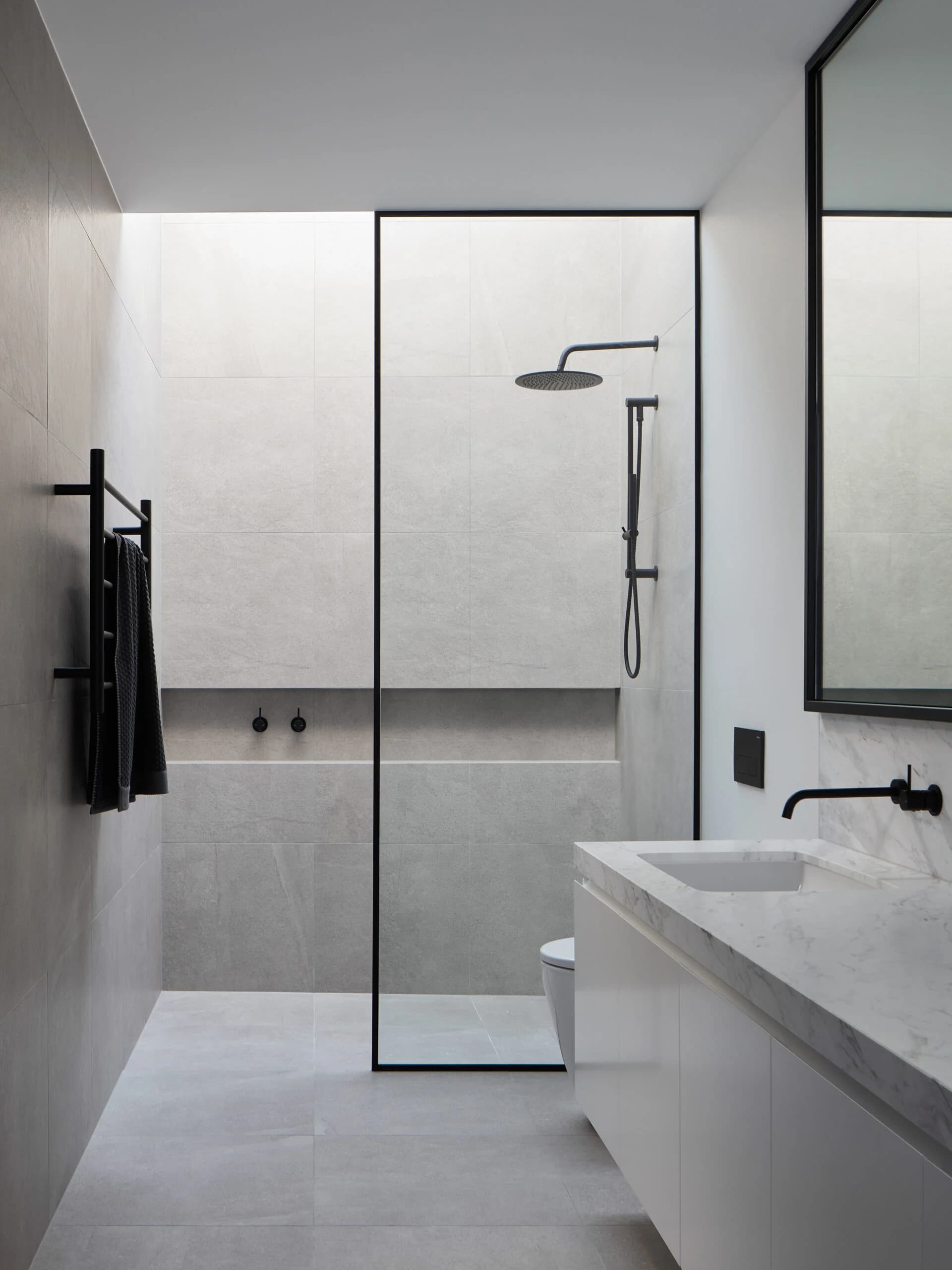 Pale tiled bathroom with a glass shower enclosure, black fittings and a long vanity.