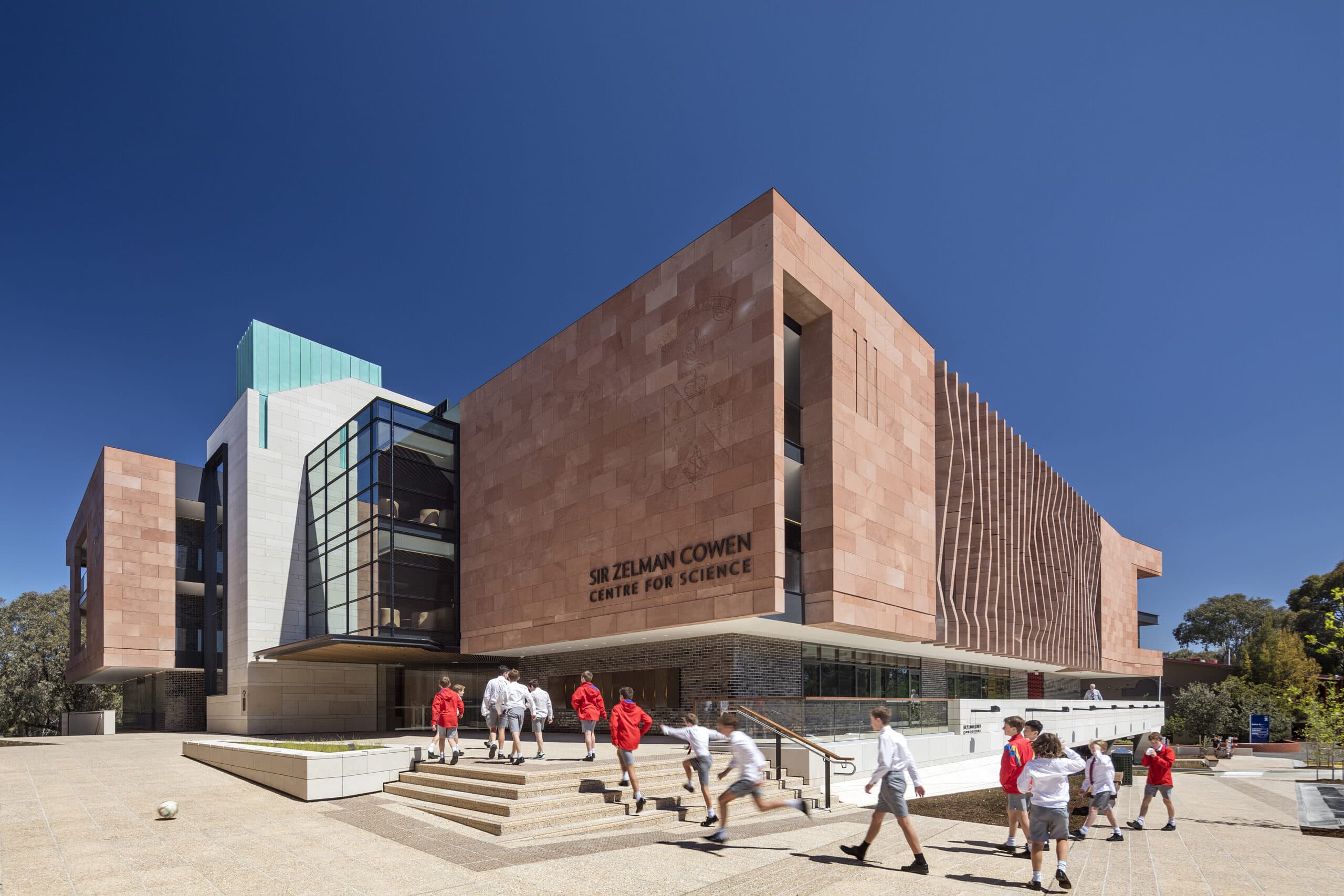 Pink stone-clad science centre with a glazed atrium, vertical facade fins and a stepped entrance forecourt.