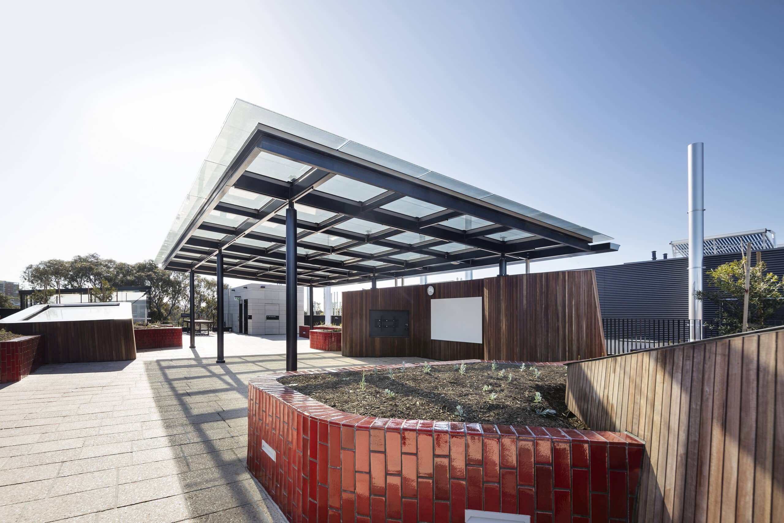Roof terrace with planted beds, timber cladding and a broad glazed canopy.