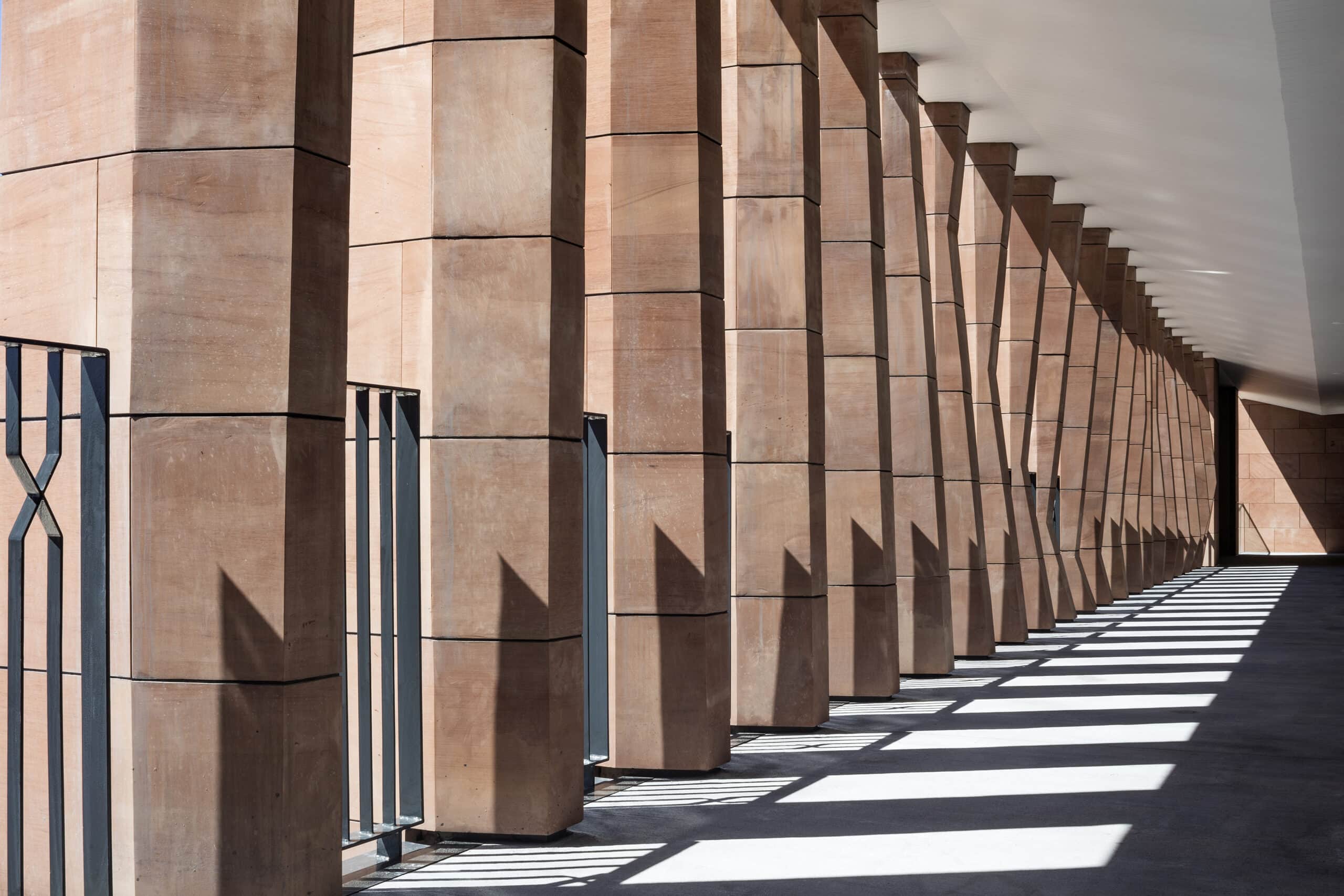 Pink stone columns casting repeated angled shadows along a covered walkway.