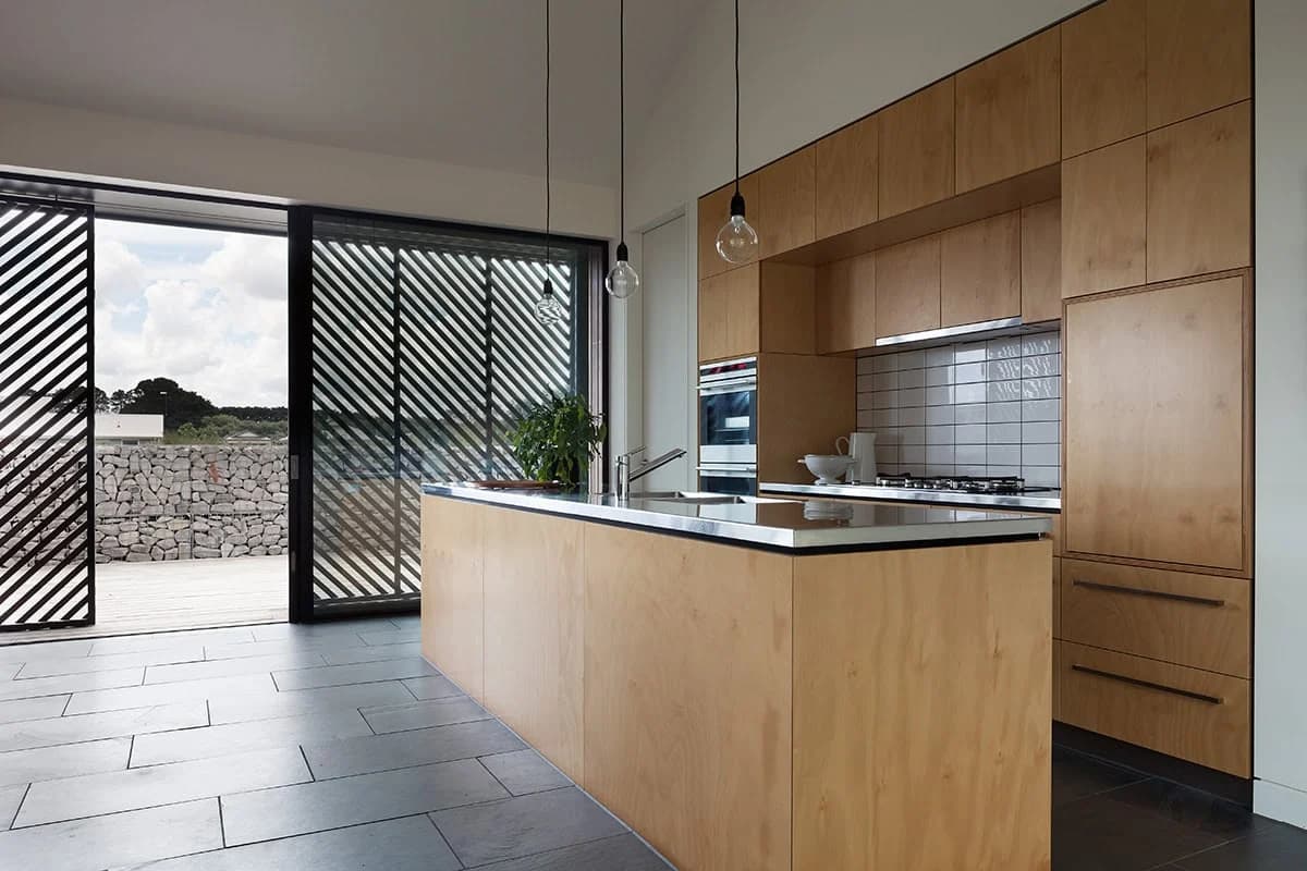 Plywood kitchen cabinetry and island beside glazed doors with diagonal timber screens.