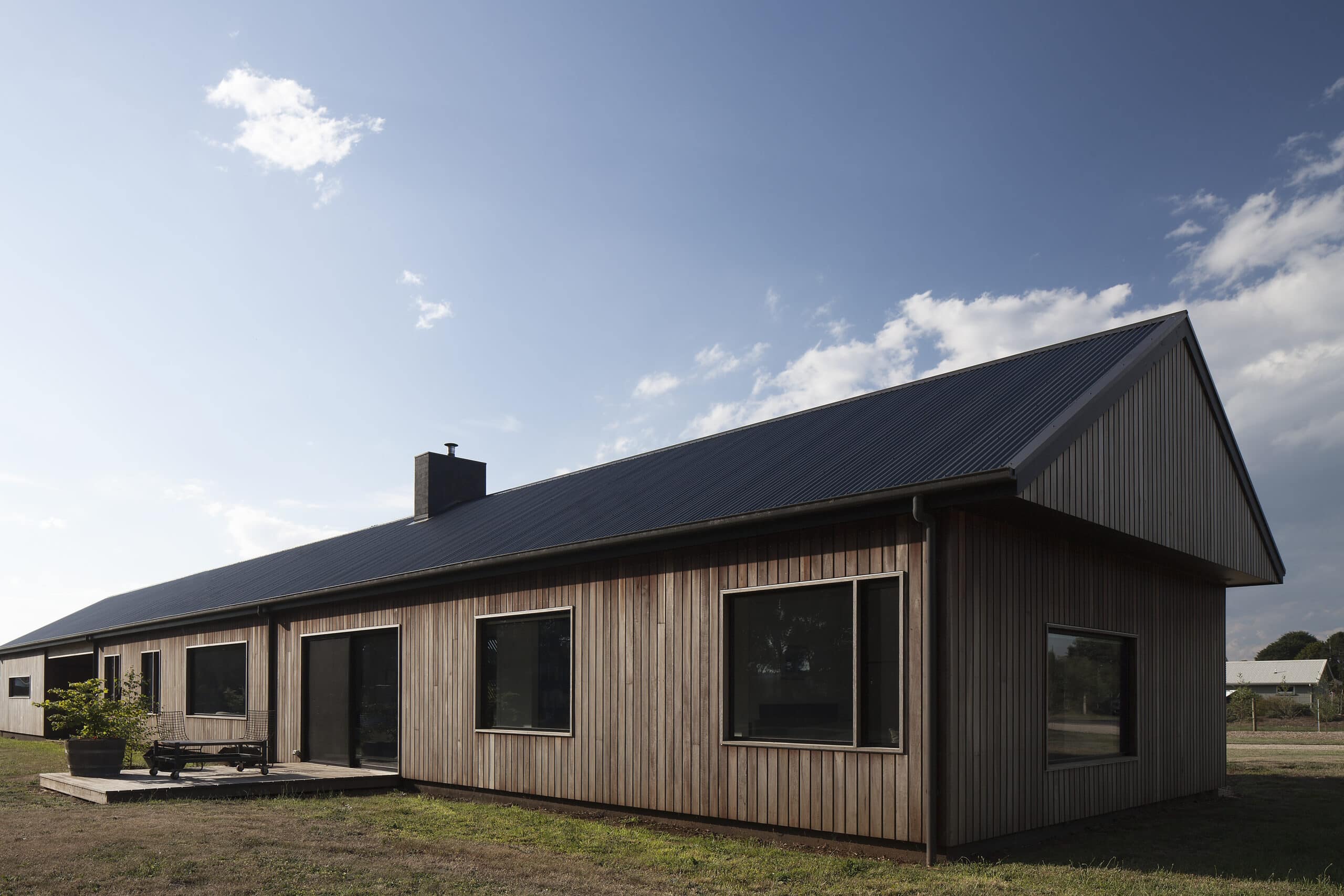 Corner view of the single-storey timber house beneath a long dark pitched roof.