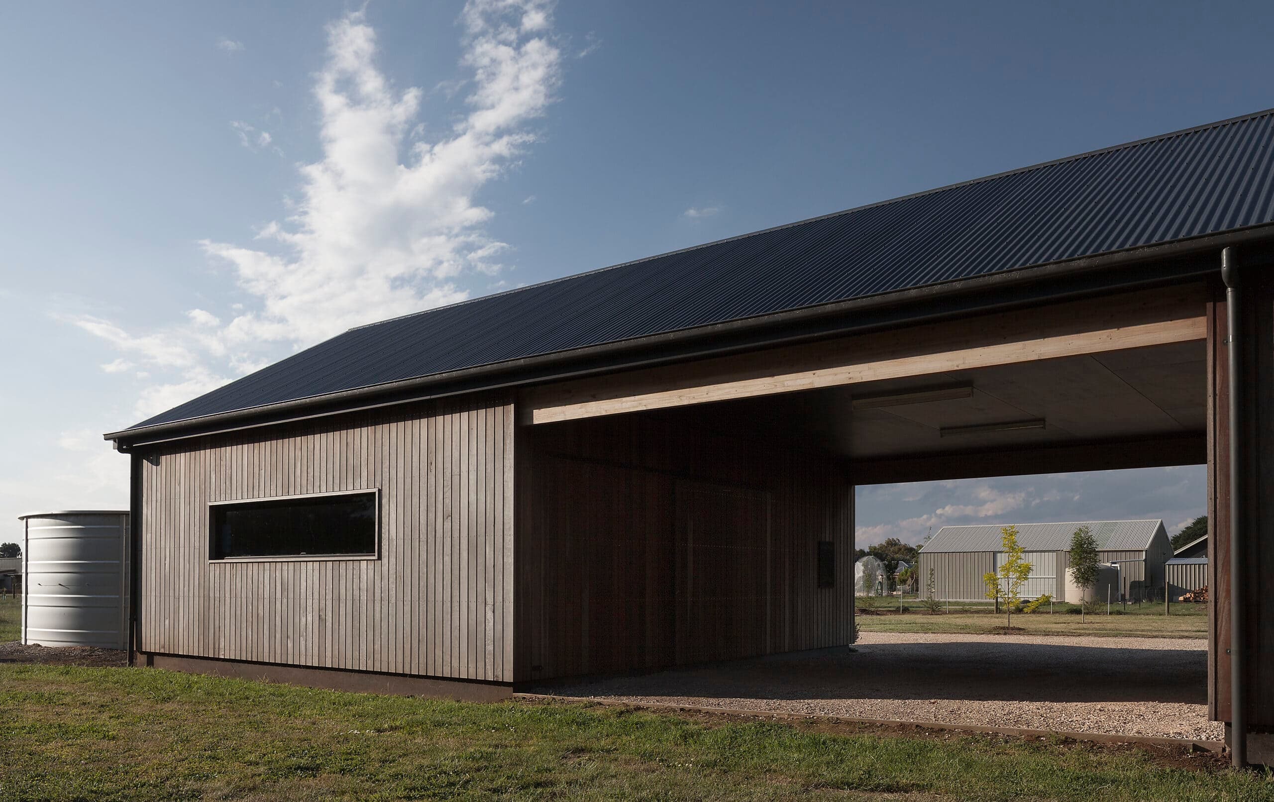 Long timber-clad building with a covered passage through its centre beneath a dark pitched roof.