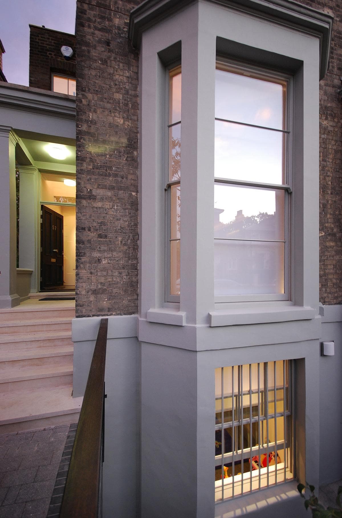 Tall white-framed bay window and entrance steps in the brick facade of Clifton Hill House.