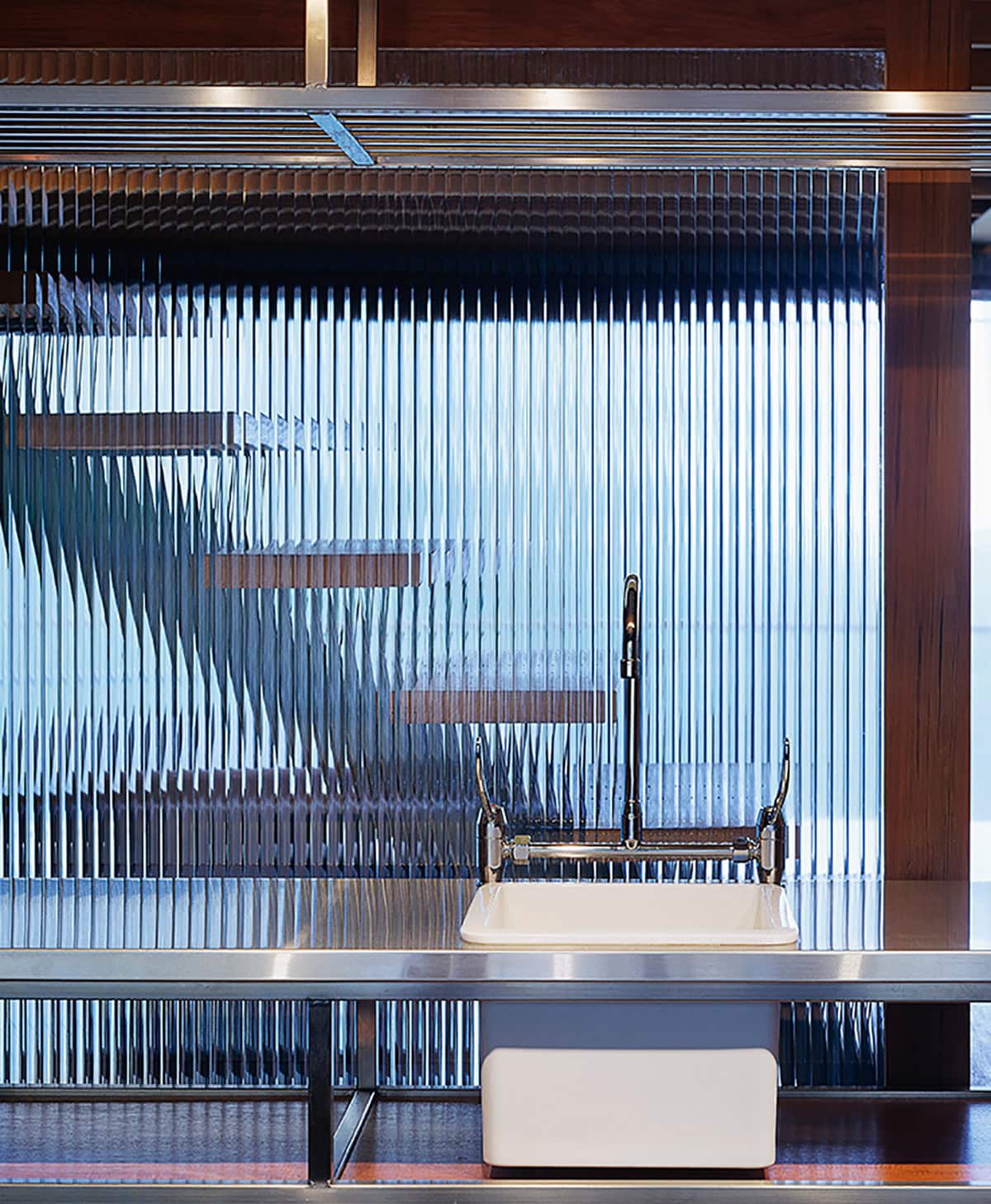 Bathroom basin and tap in front of ribbed translucent glazing framed by timber.