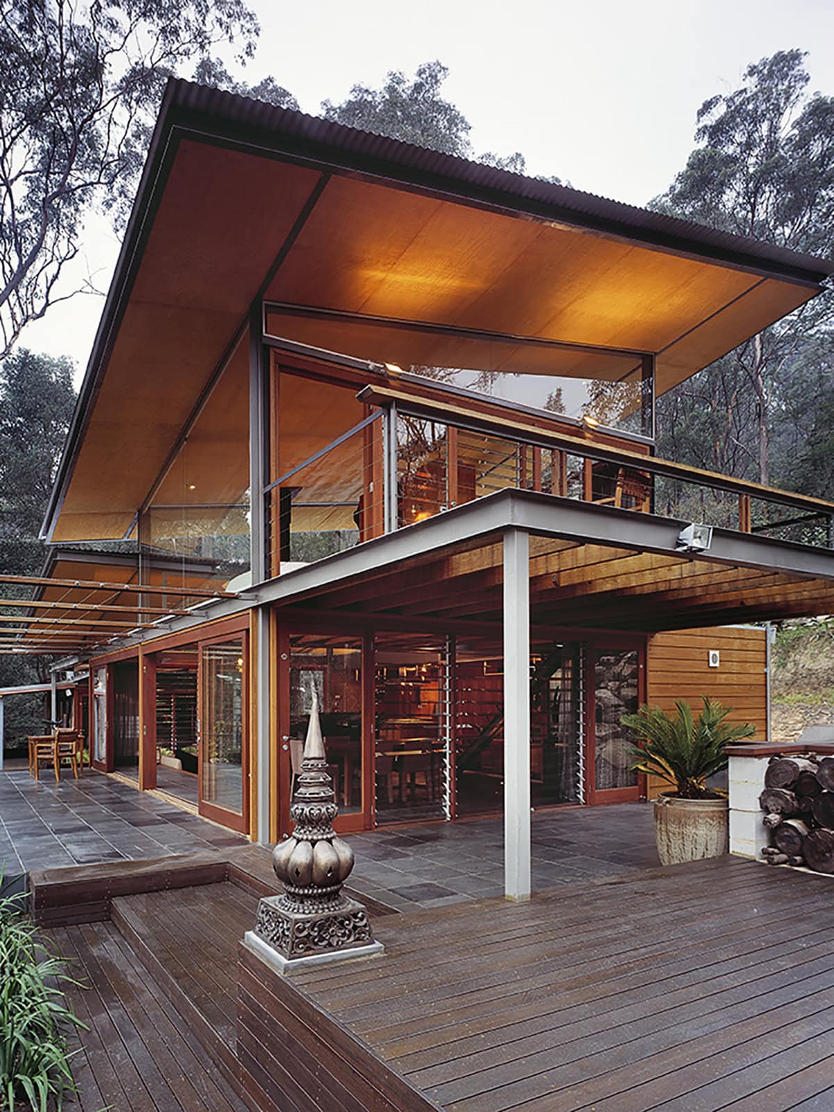 Two-storey timber and glass house with broad projecting roofs and decks among trees.