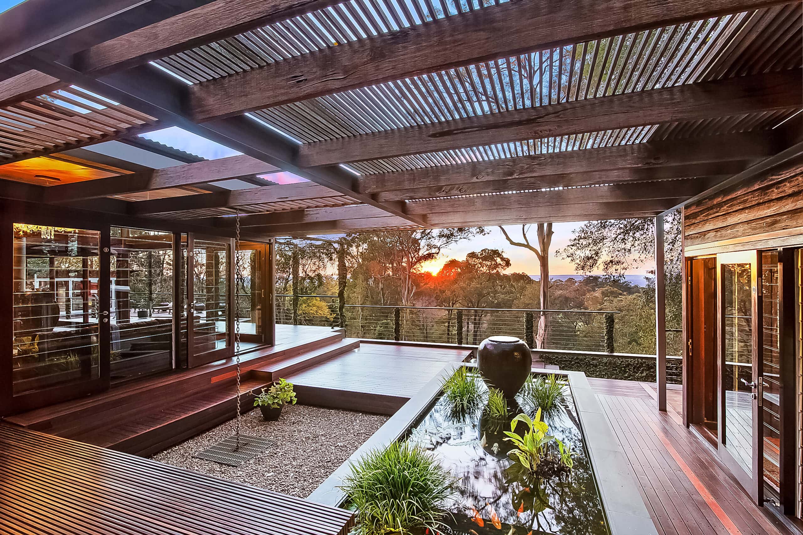 Sheltered timber courtyard with a planted water feature and views through the trees at sunset.