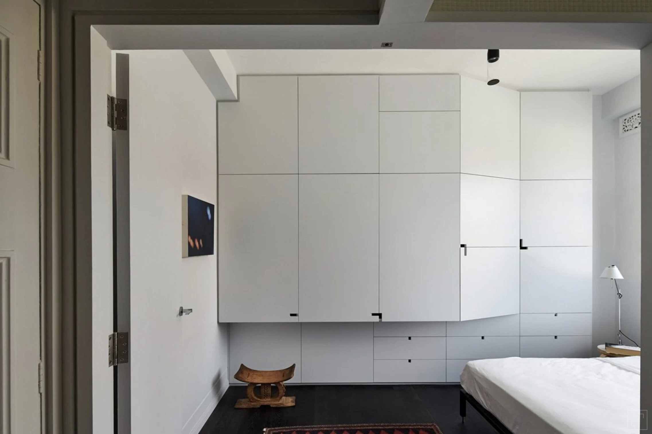 White bedroom with geometric fitted storage wrapping around the corner above a dark timber floor.