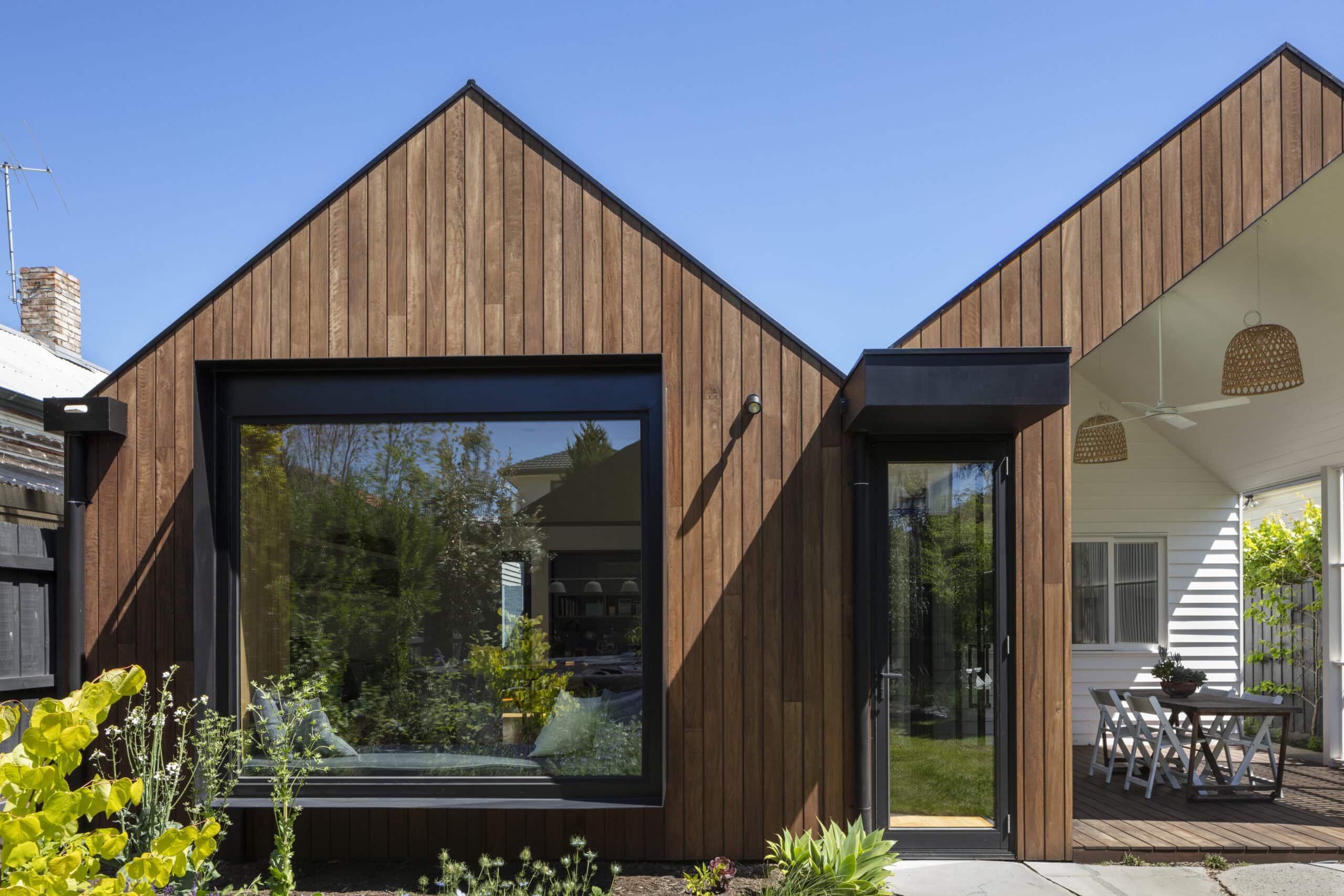Twin pitched timber-clad extensions with large black-framed windows opening towards a planted garden.